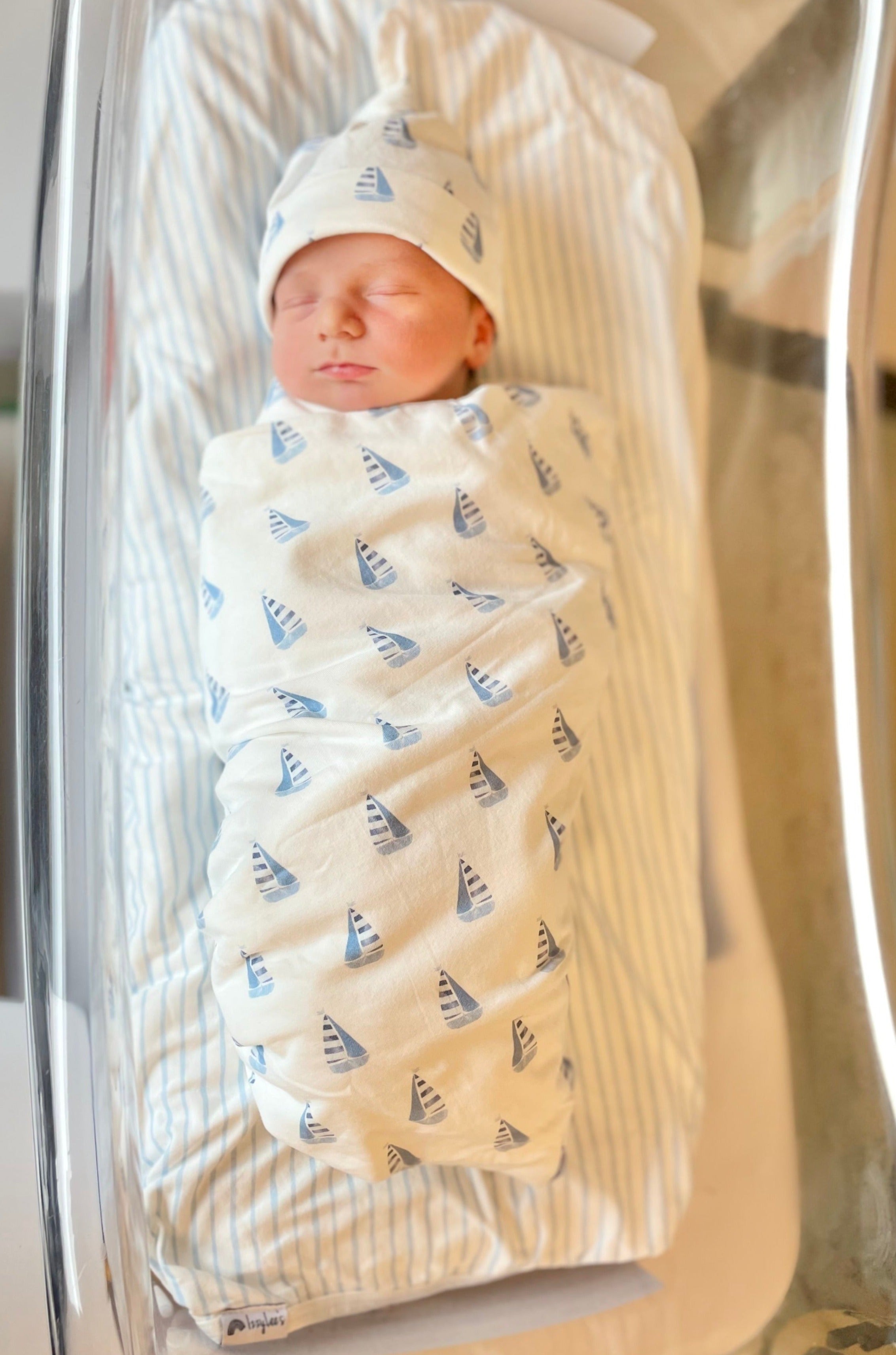Newborn baby swaddled in a blanket with sailboat pattern, wearing a matching hat.
