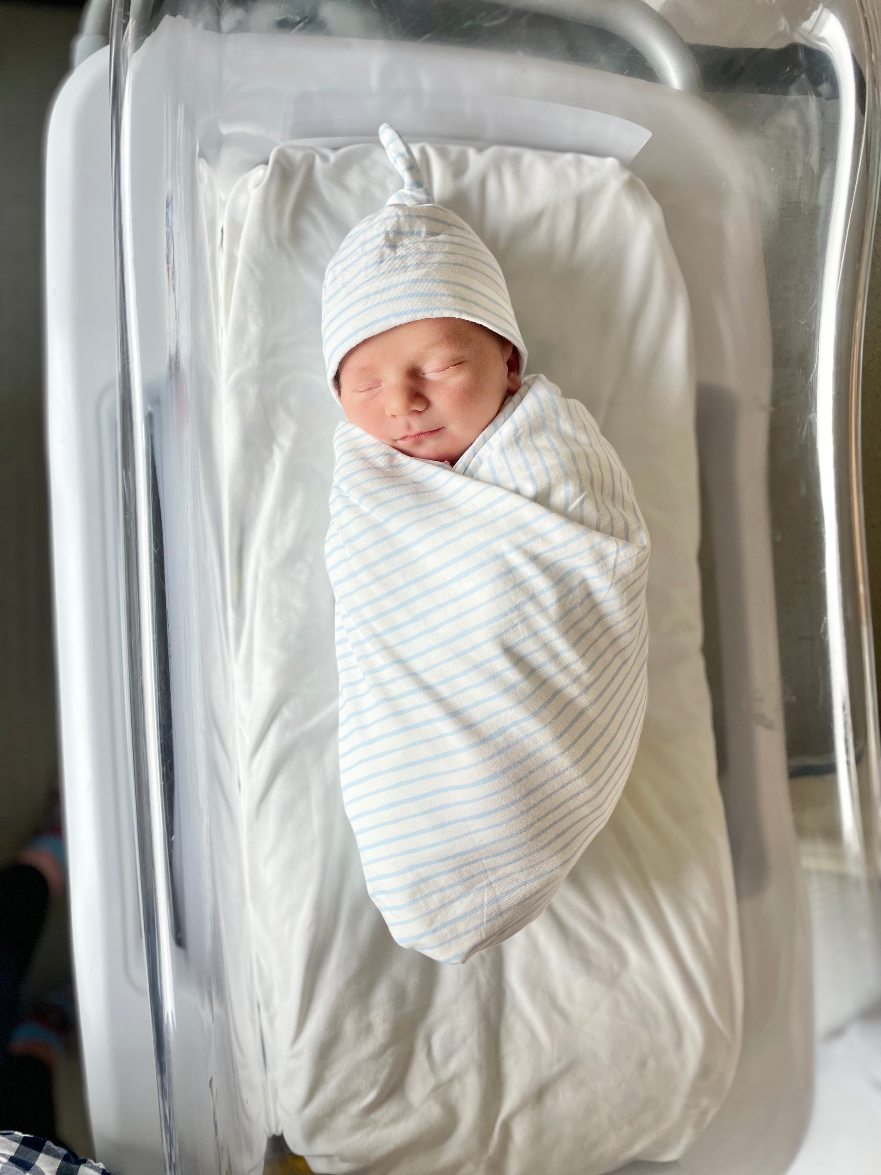 Newborn baby swaddled in white blanket and cap in hospital crib
