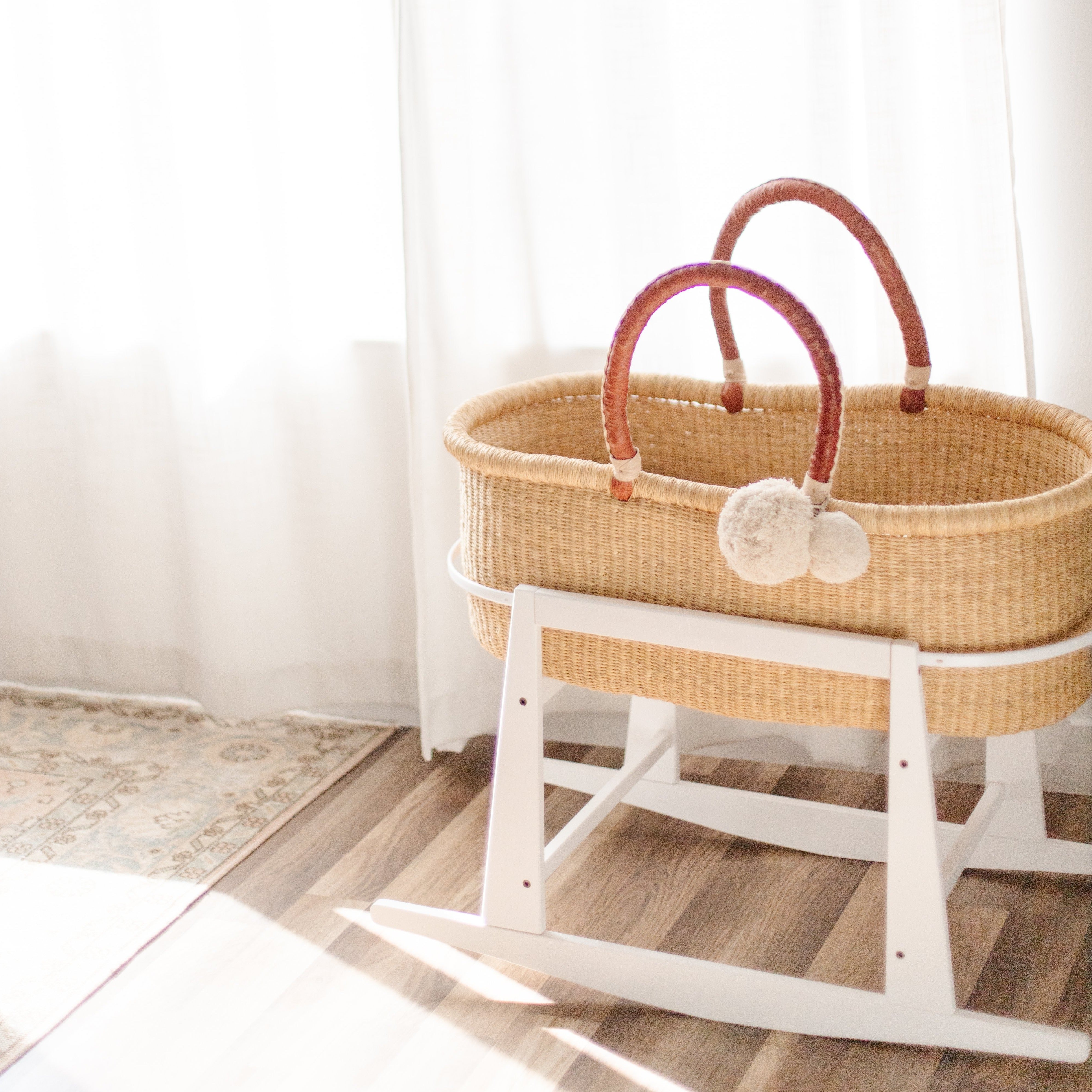 Wicker baby Moses basket on a white stand in a softly lit room.