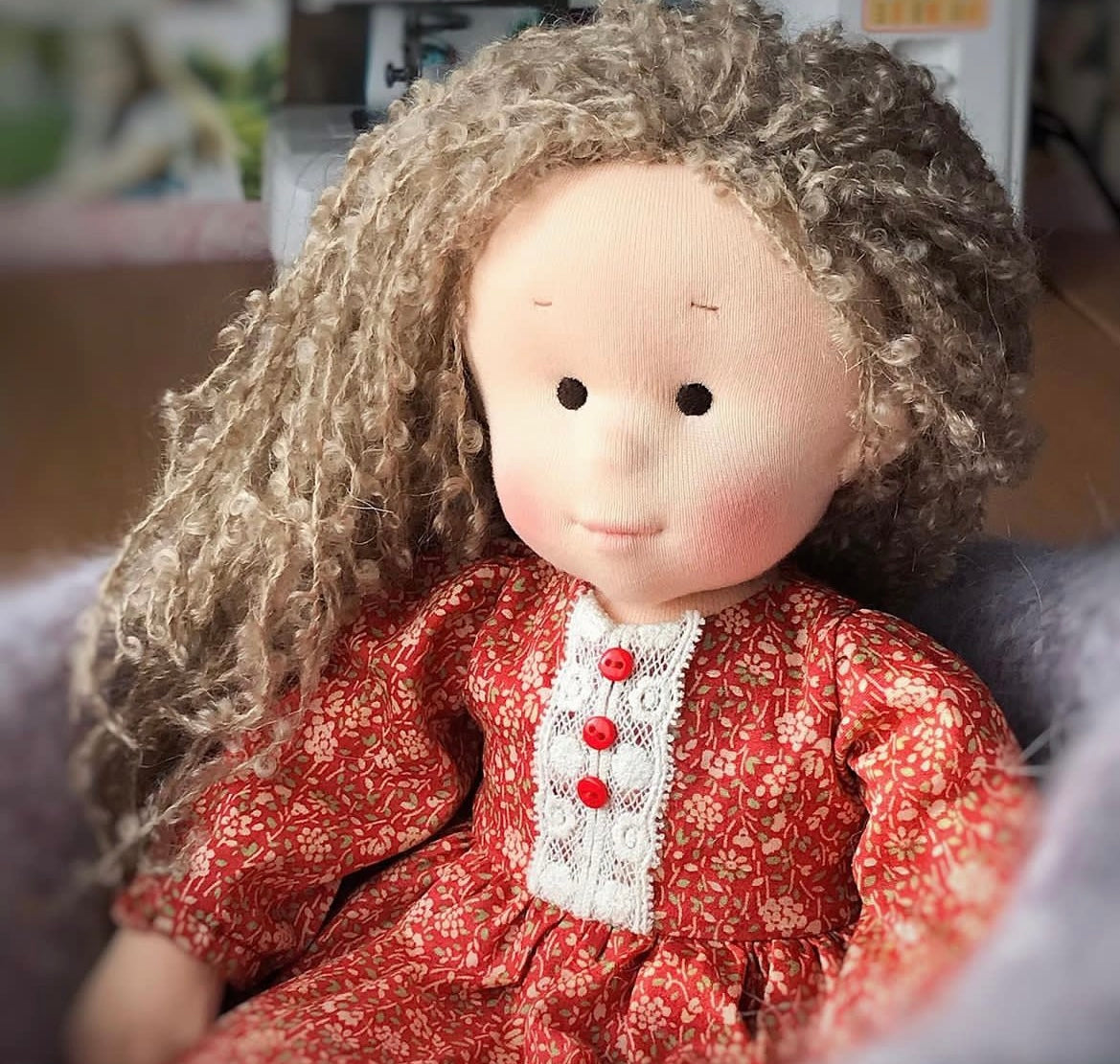 Textile doll with curly hair wearing a red dress with white lace details.