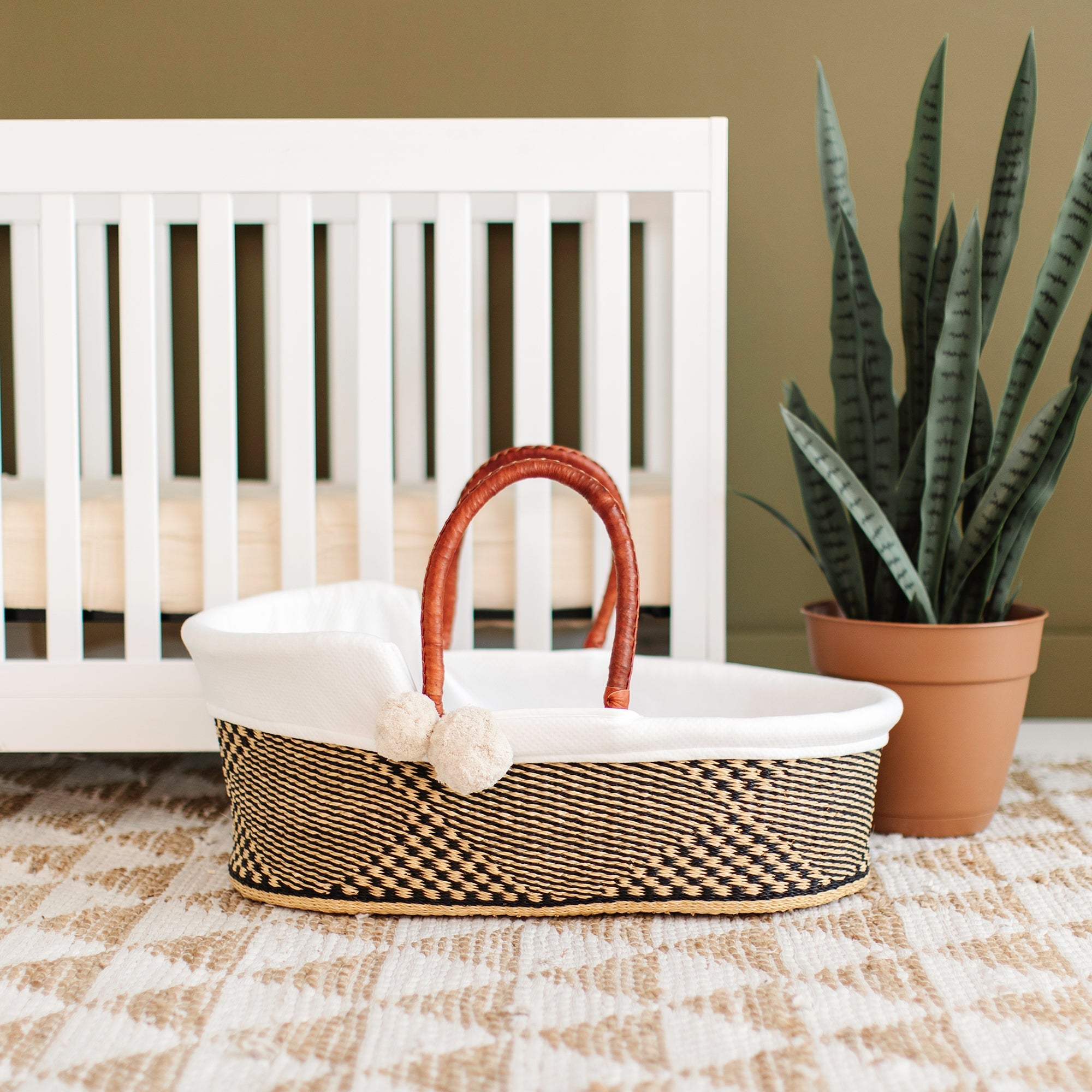 Woven basket with a white lid on a checkered floor in front of a white crib.