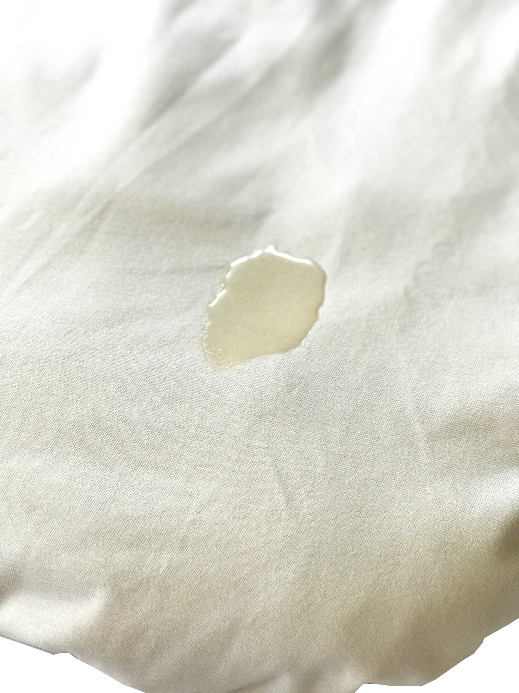 Close-up of a white fabric with a small yellowish stain on a white background
