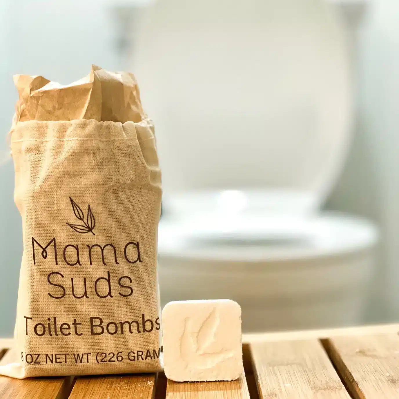 Mama Suds Non-Toxic Toilet Cleaning Tablets sitting on the wooden bench in front of a white toilet.