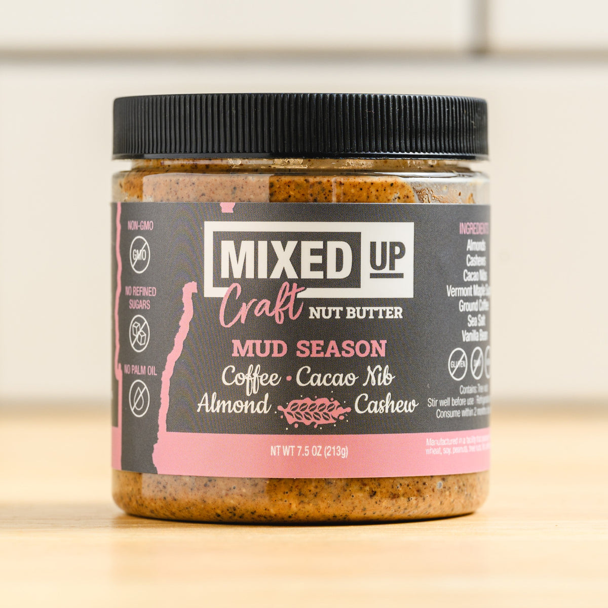 Jar of Mixed Up Craft Nut Butter with a black lid on a wooden surface