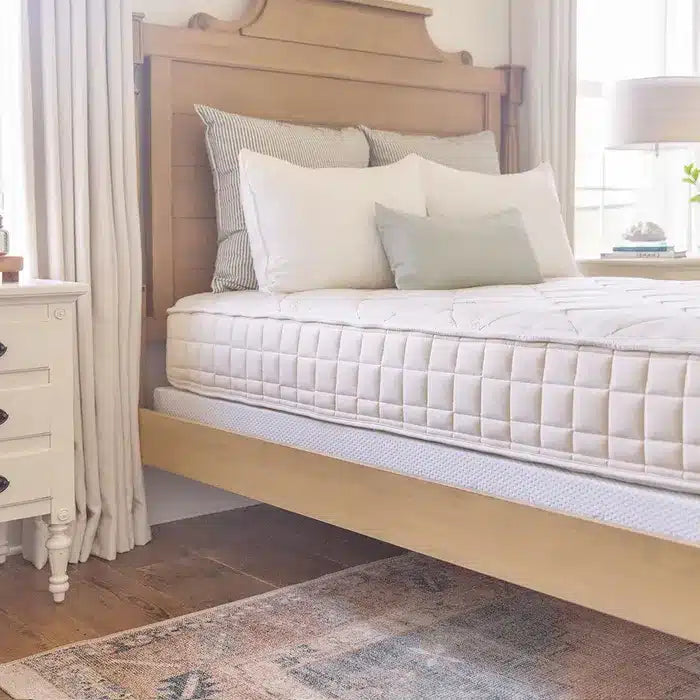 White bed with pillows in a room with curtains and a side table