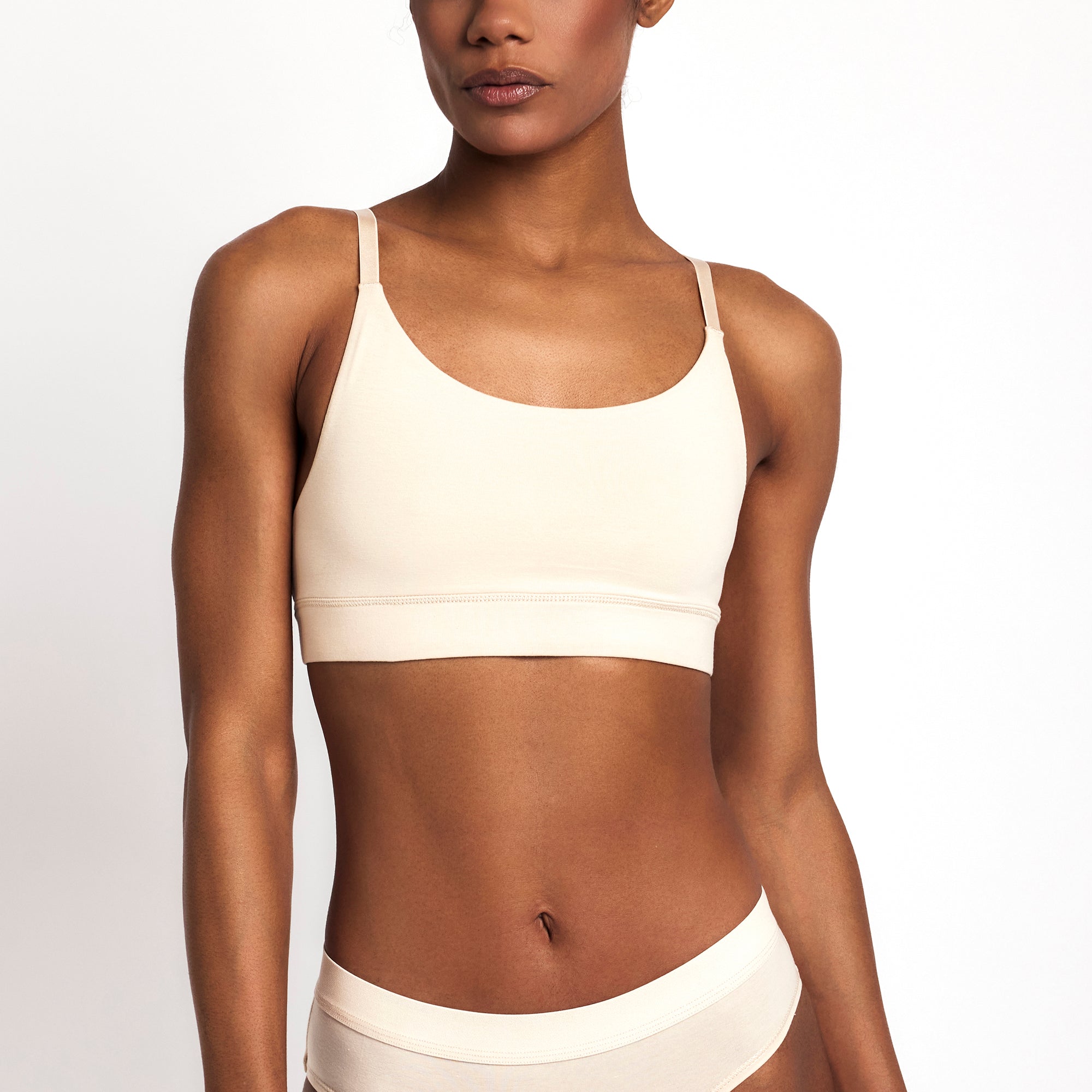 Woman wearing a white sports bra and underwear set on a plain background