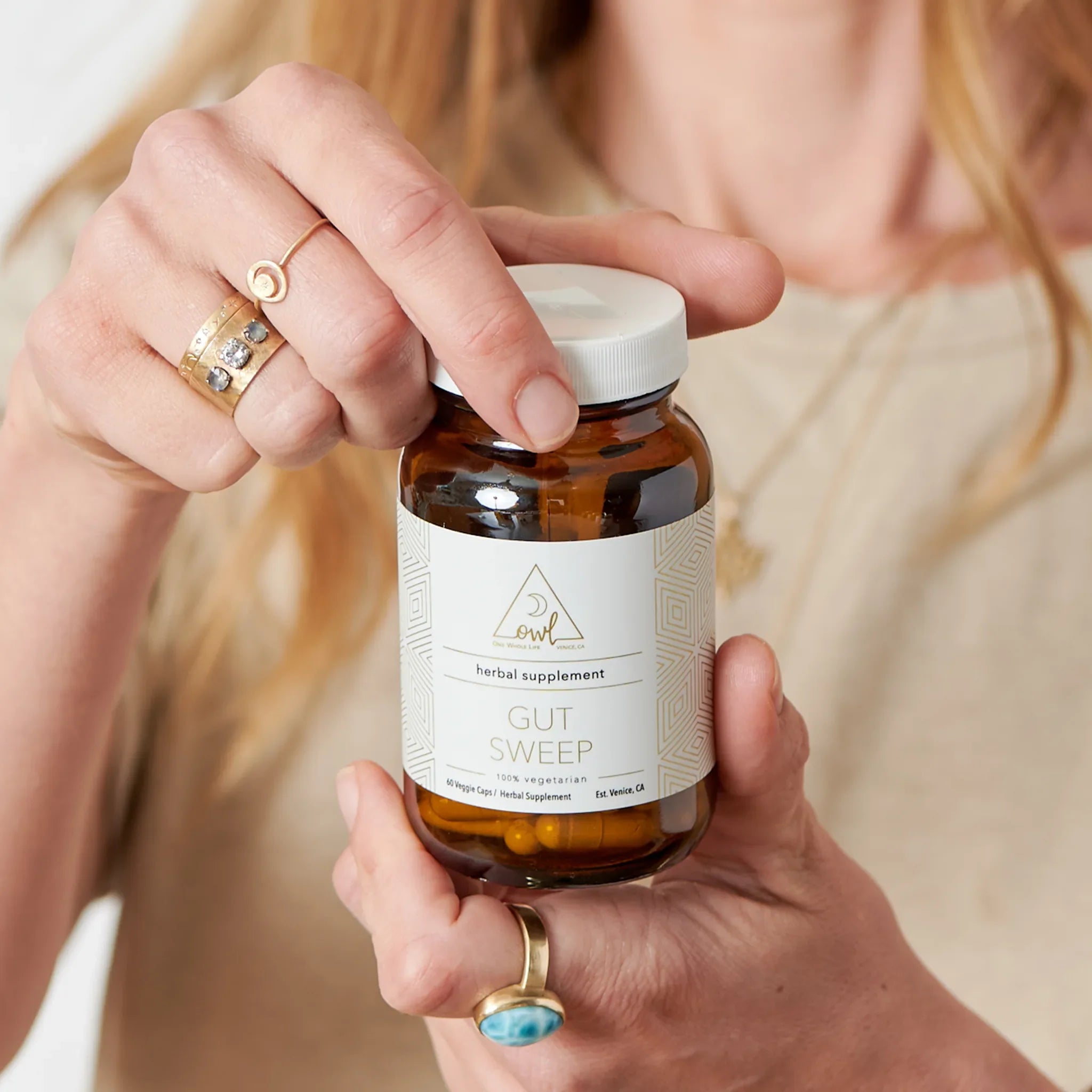 Person holding a bottle of 'Gut Sweep' herbal supplement with a white label.
