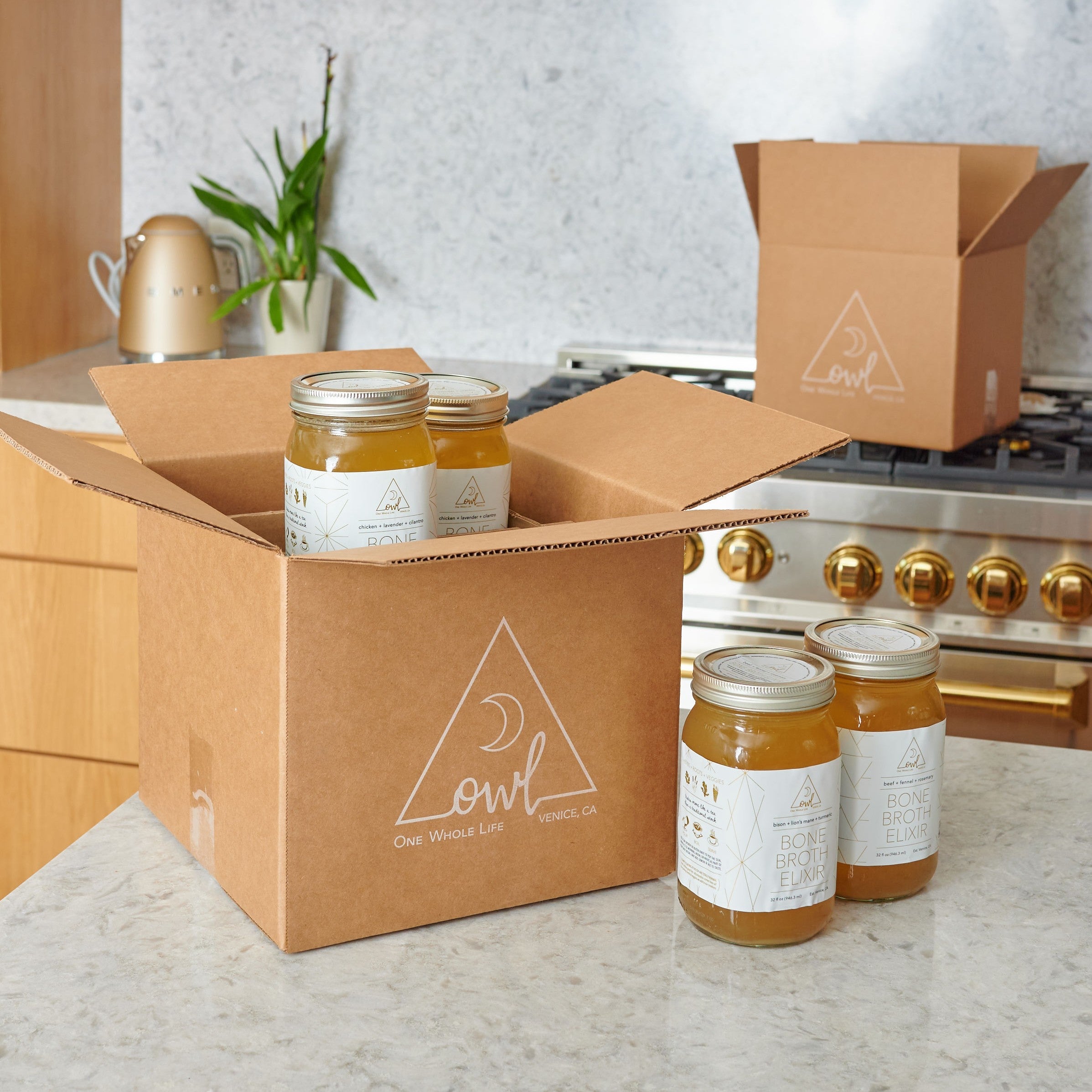 Open cardboard box with jars of honey on a kitchen counter, featuring the 'One Owl Pantry' logo.