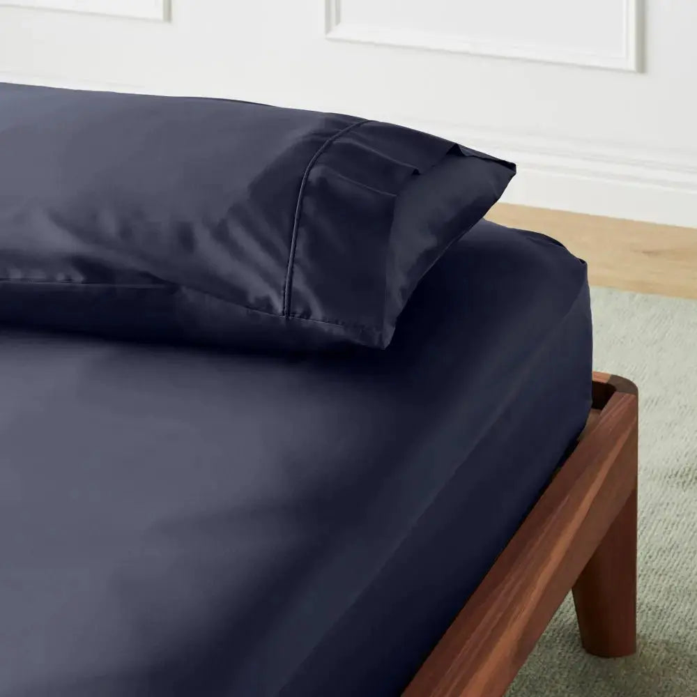 Navy blue bed sheets and pillow on a wooden bed frame with a neutral background