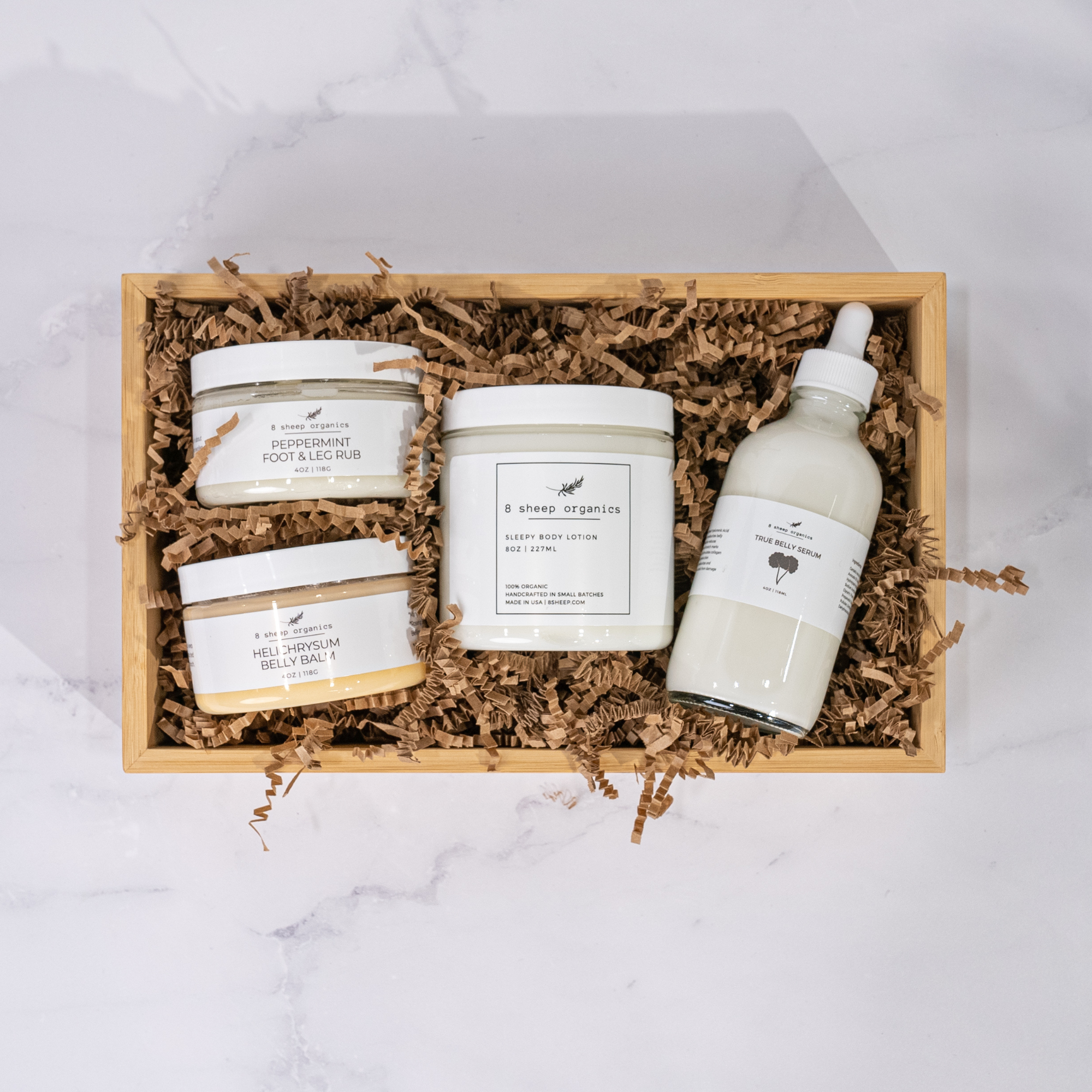 Set of skincare products including jars and a bottle in a wooden box on a marble surface.