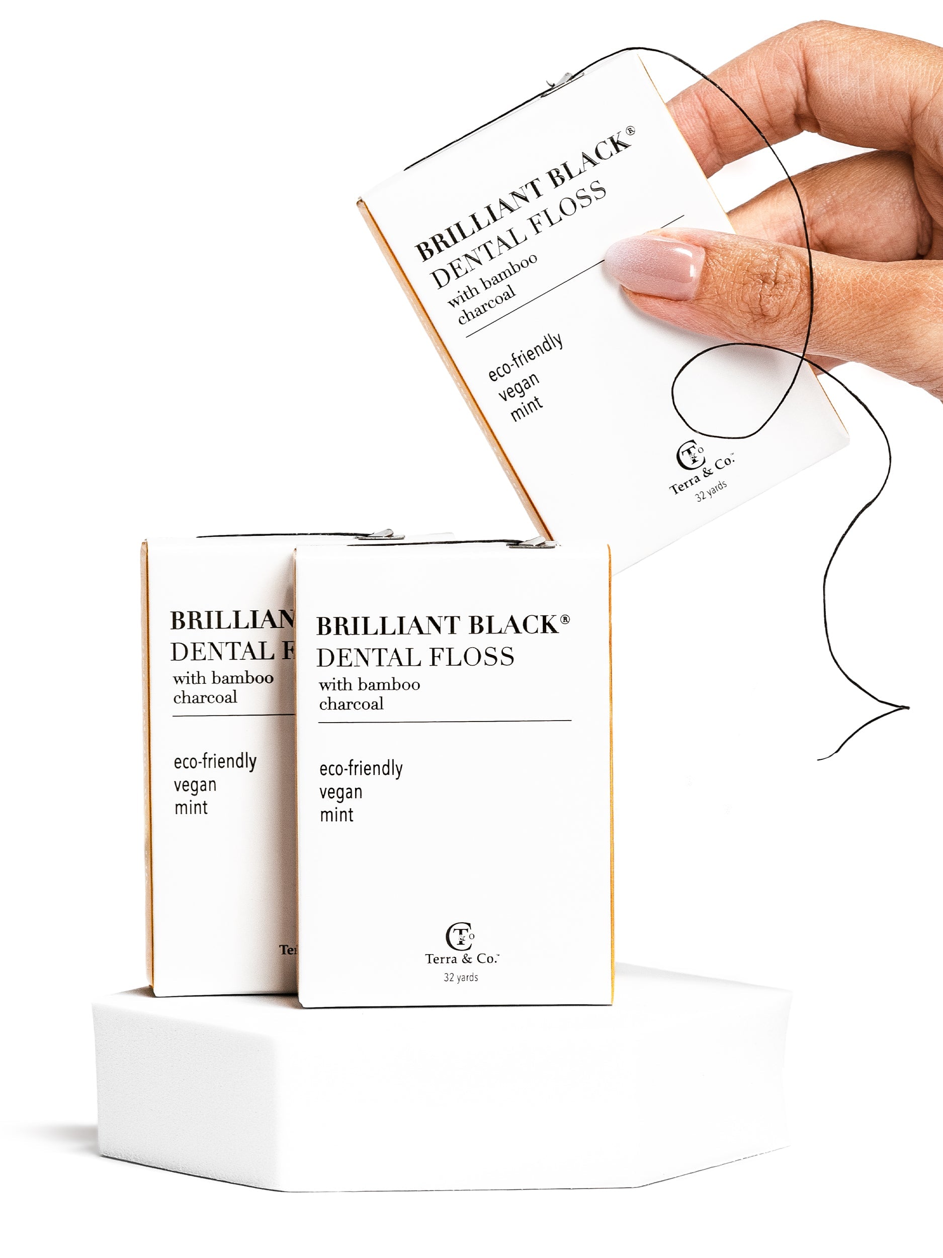Hand holding a box of Brilliant Black dental floss with packaging in the background.