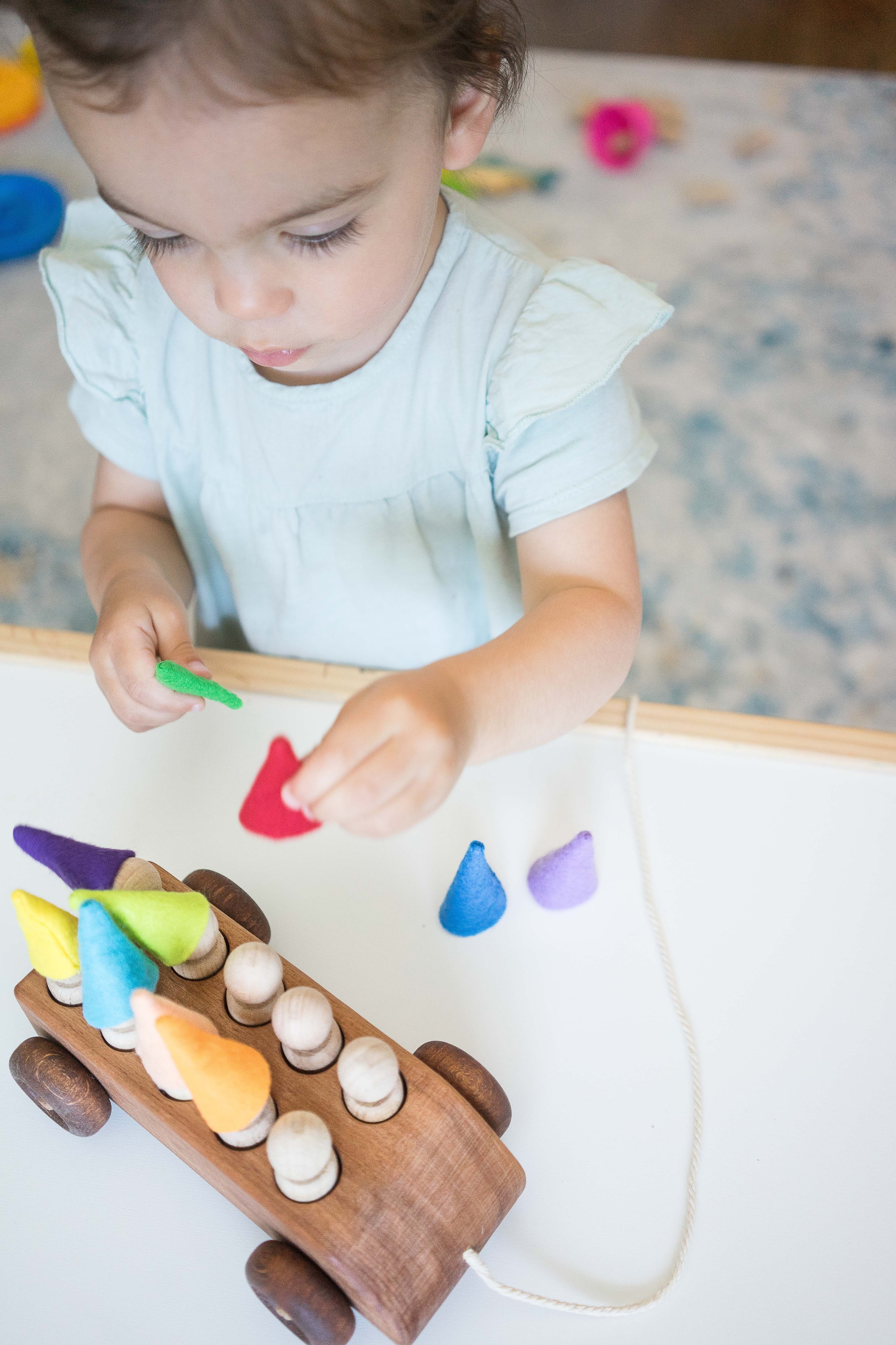 Child playing with a wooden toy featuring colorful pegs on a light surface.