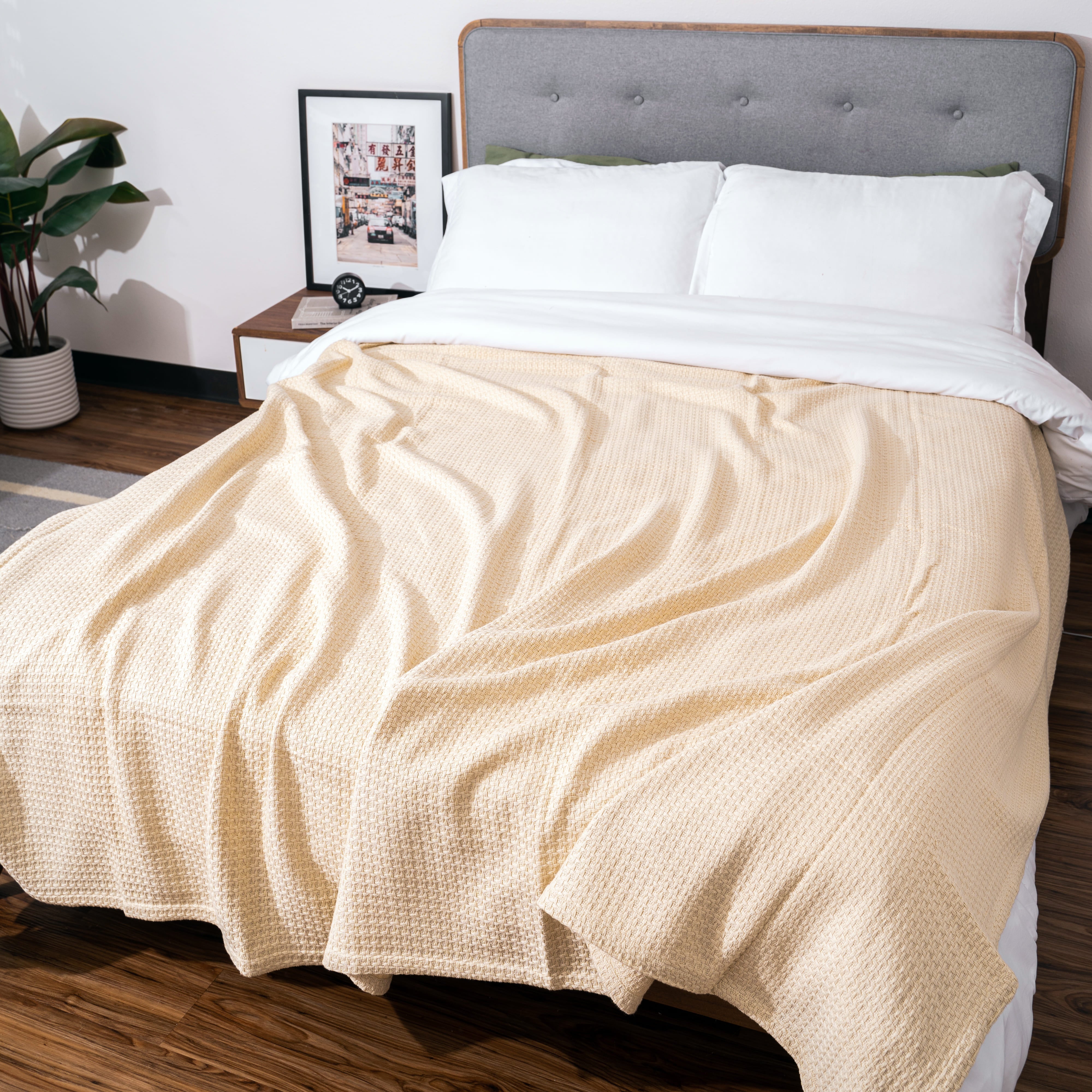 Beige blanket draped over a bed with white pillows and a gray headboard.