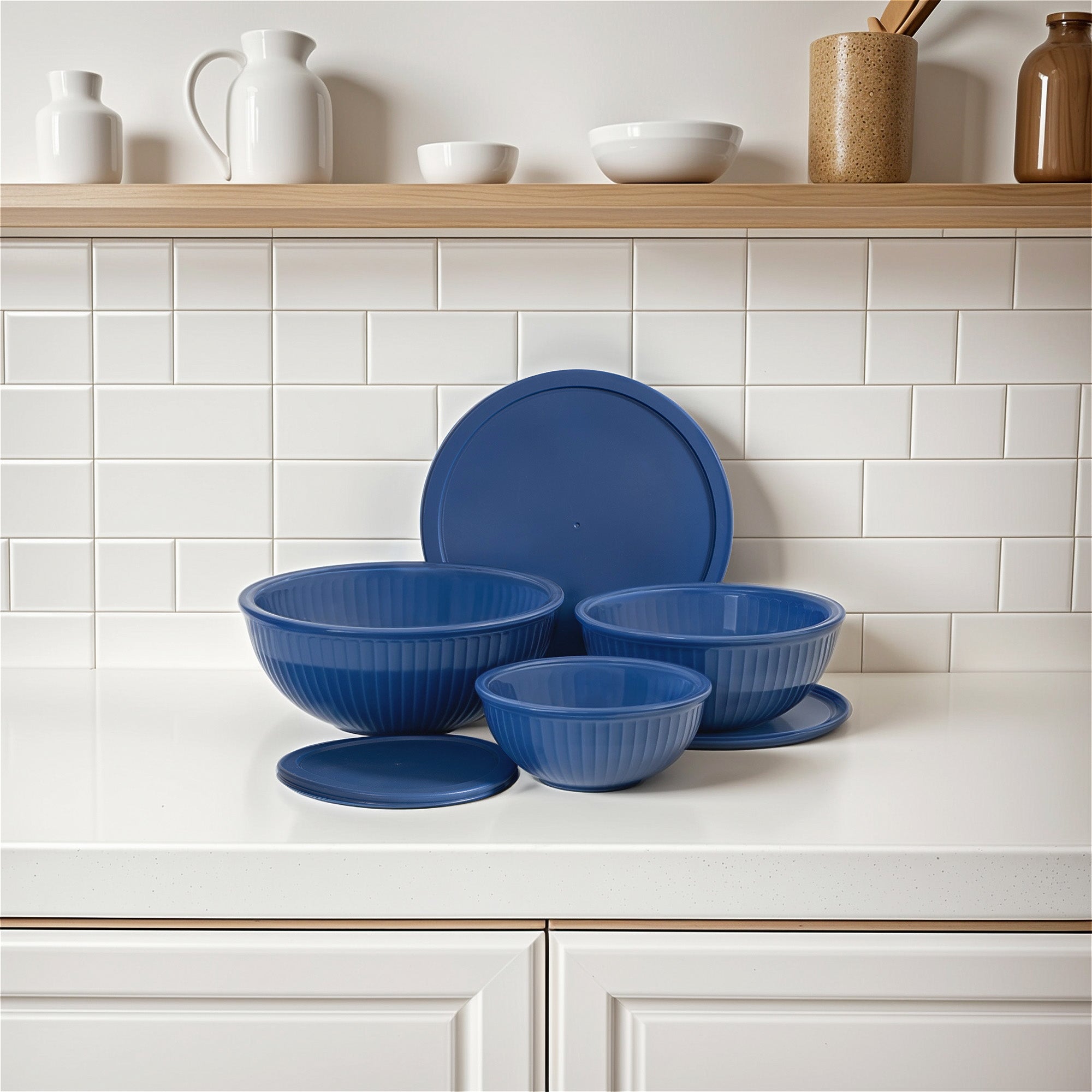 Set of blue ceramic bowls on a kitchen counter with white tiled wall and wooden shelves in the background.