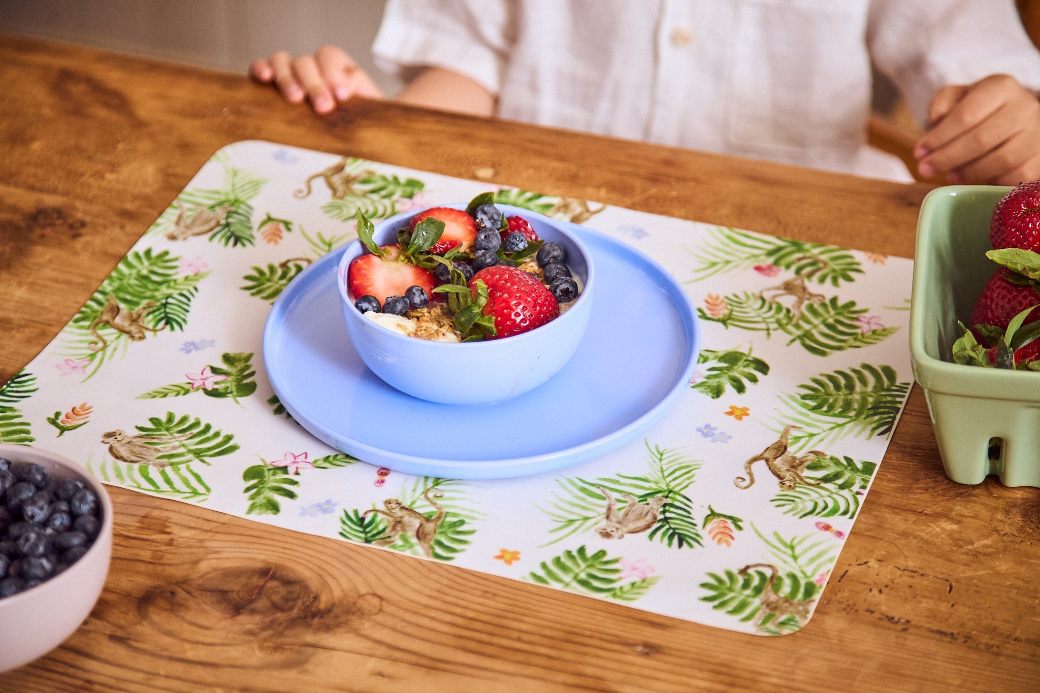 Bowl of berries on a floral placemat with a child's hands in the background