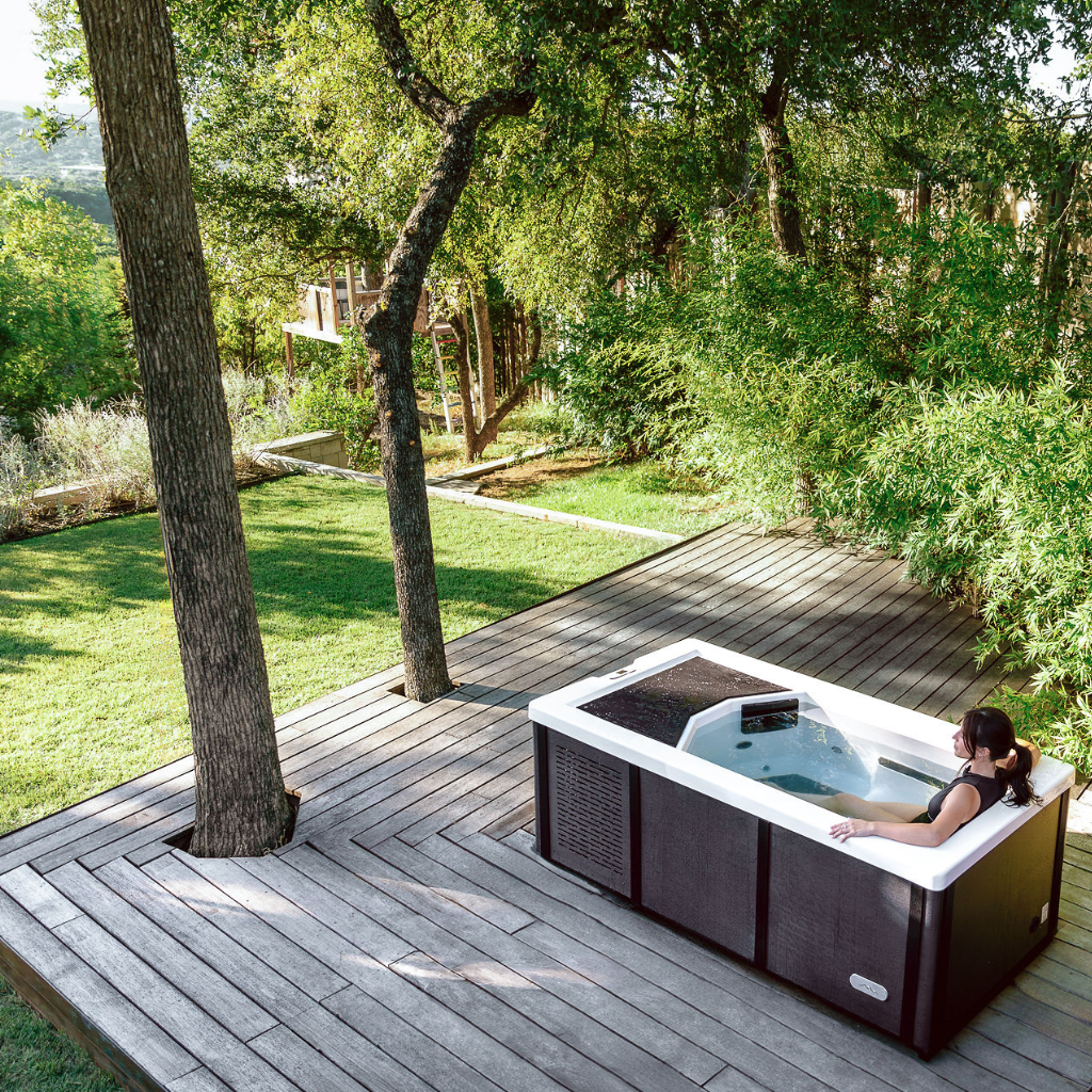 Person relaxing in a hot tub on a wooden deck surrounded by greenery