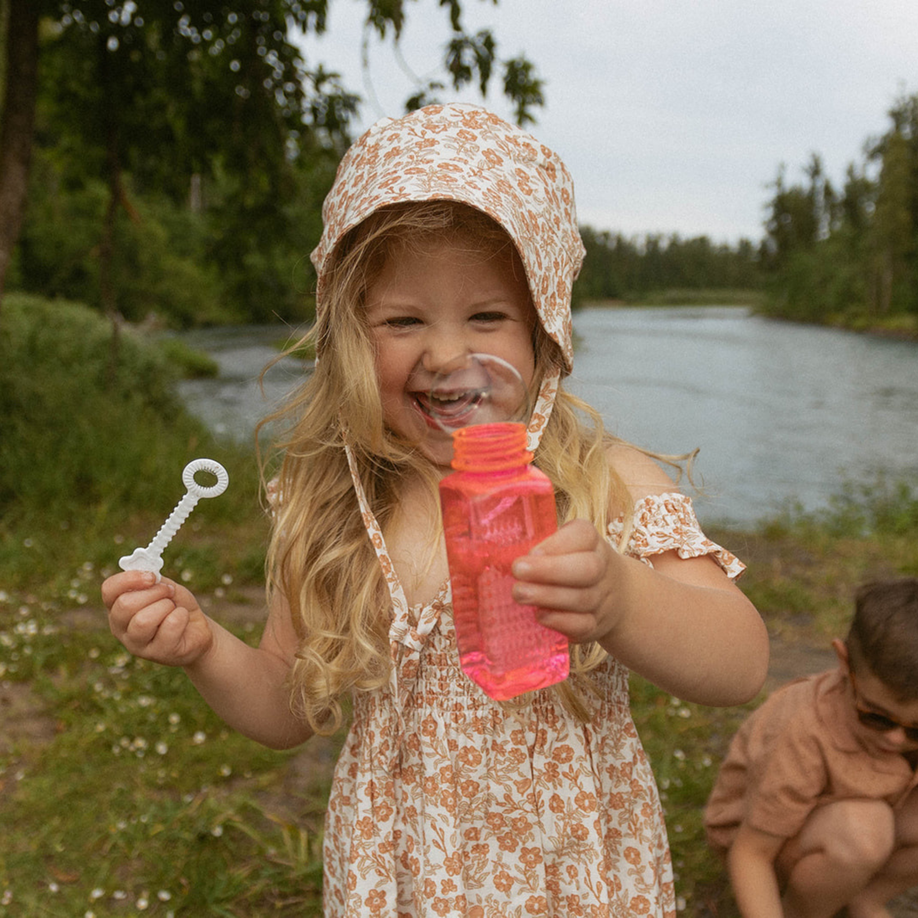 Child playing with bubbles outdoors near a body of water