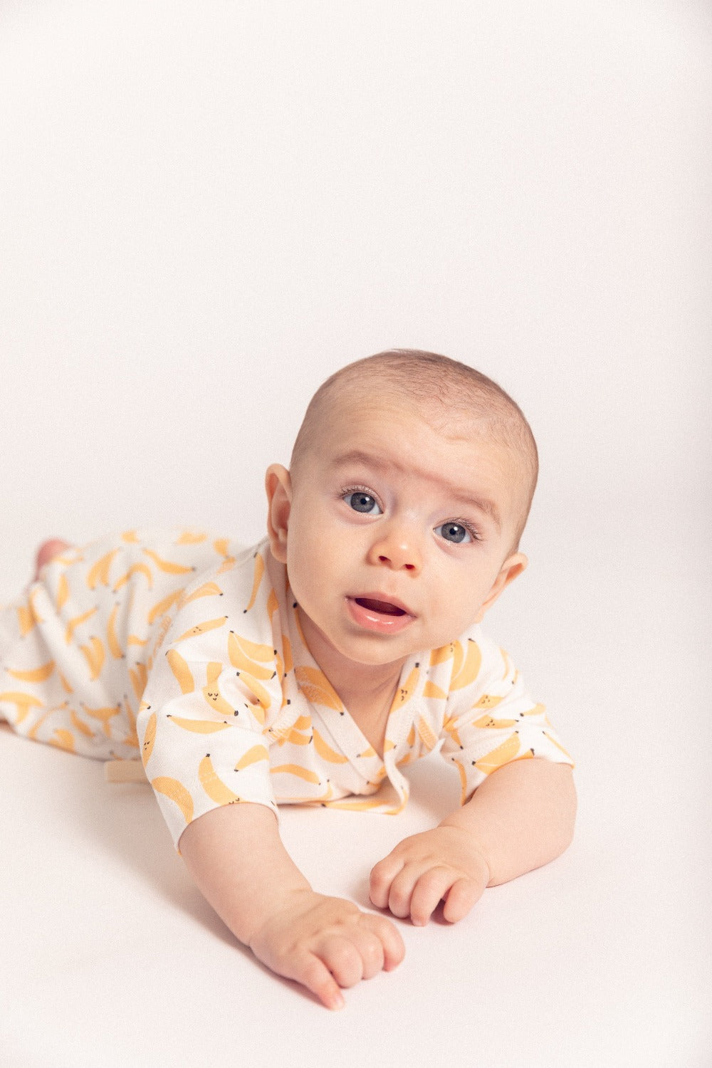 Baby wearing a white onesie with yellow patterns on a light background