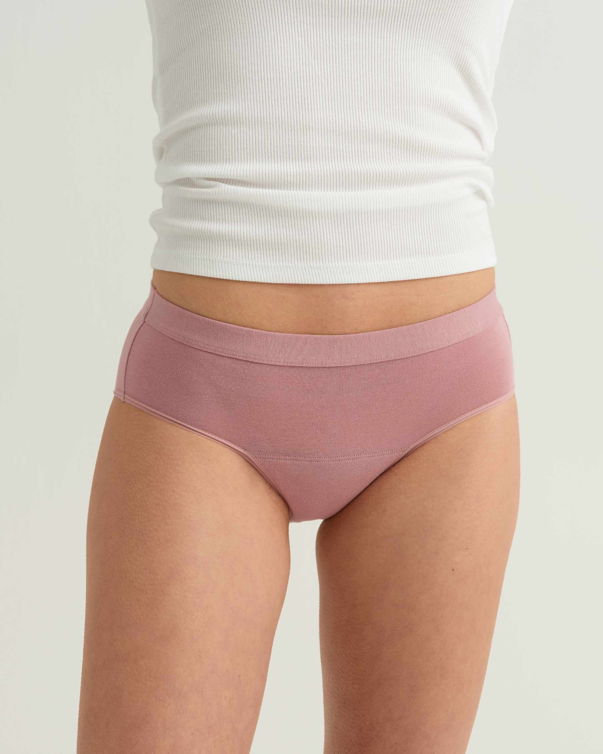 Person wearing pink underwear and a white top on a plain background