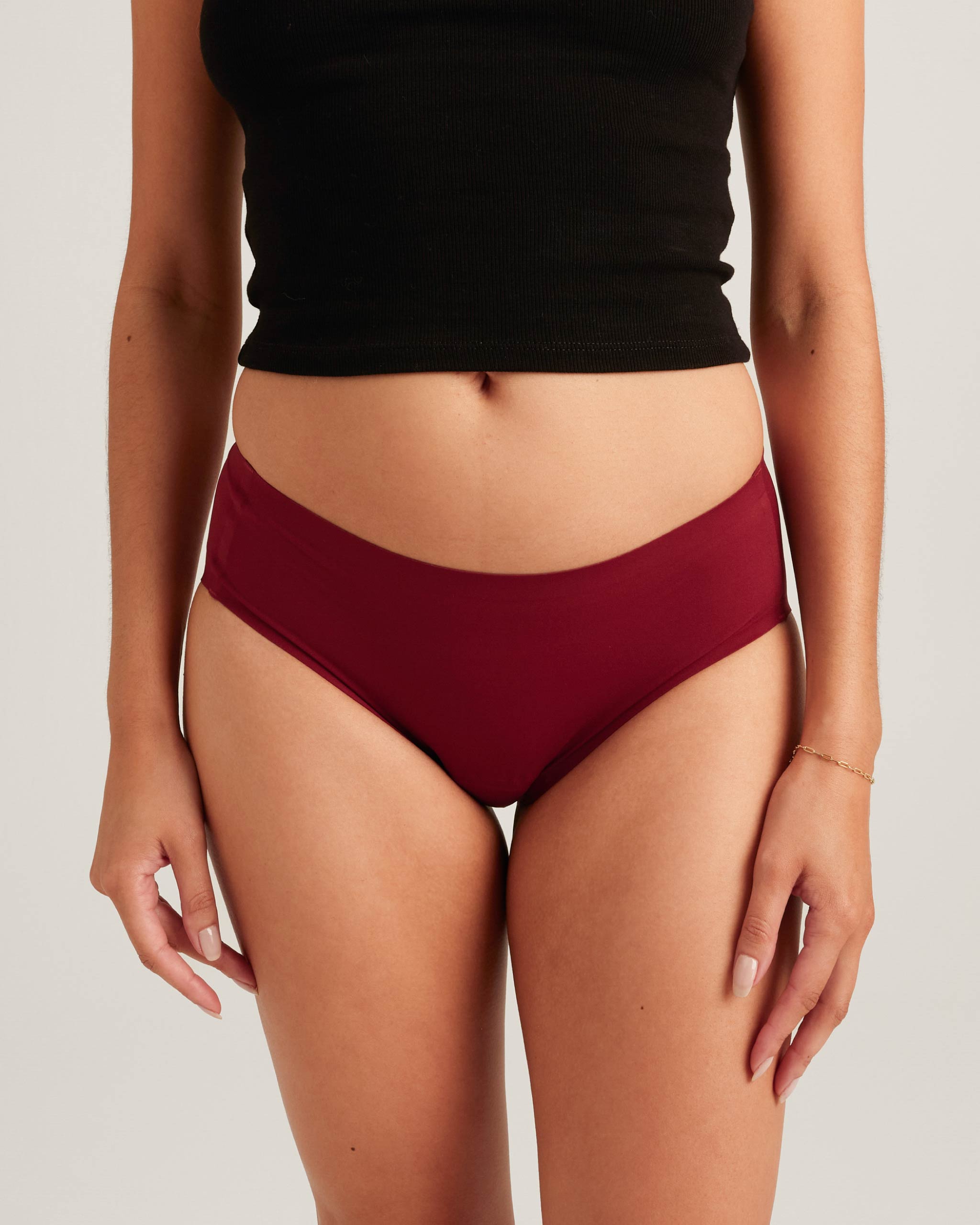 Person wearing maroon high-waisted bikini bottoms and a black top on a light gray background