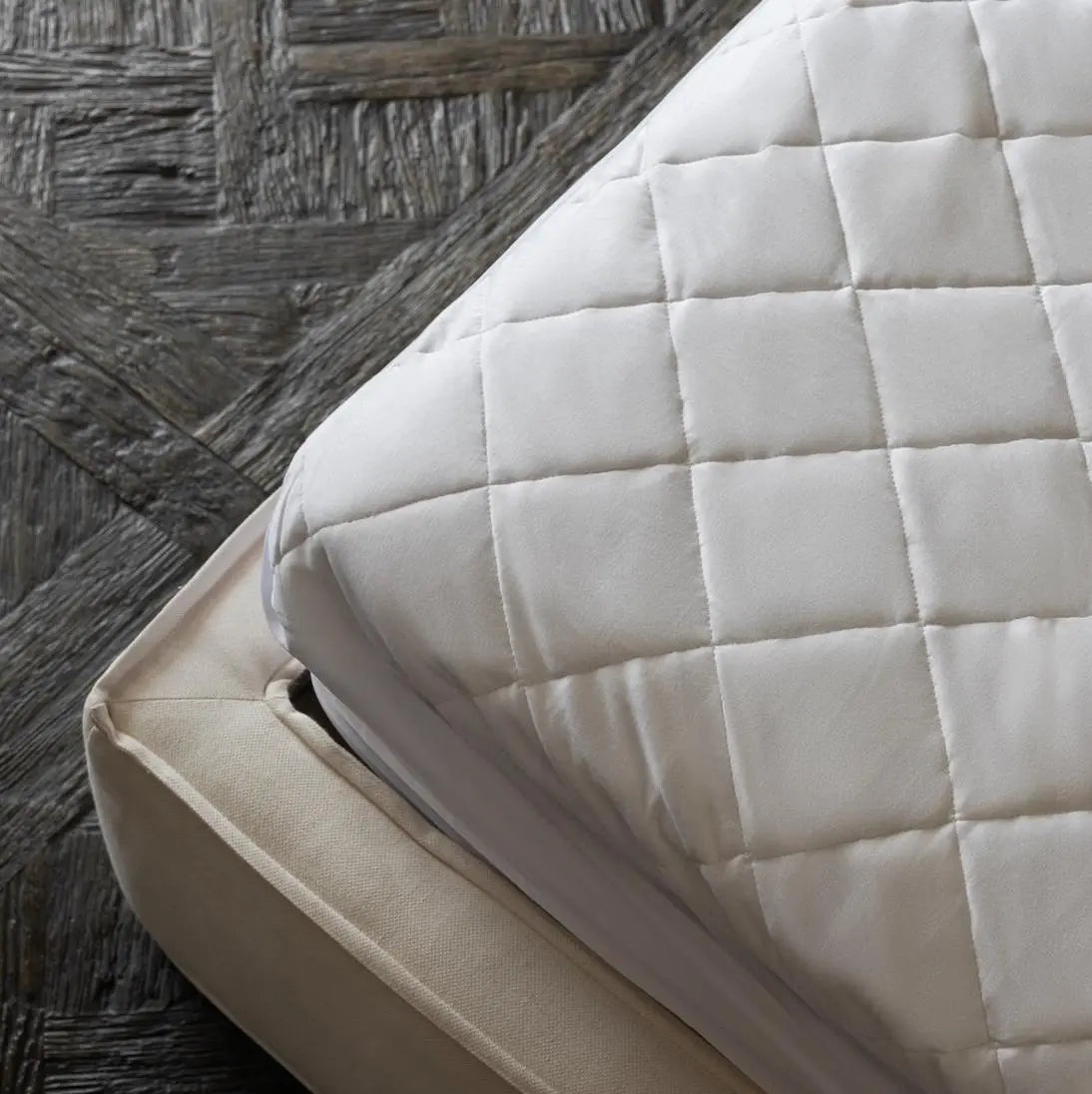 Close-up of a quilted mattress cover on a bed with a wooden floor.