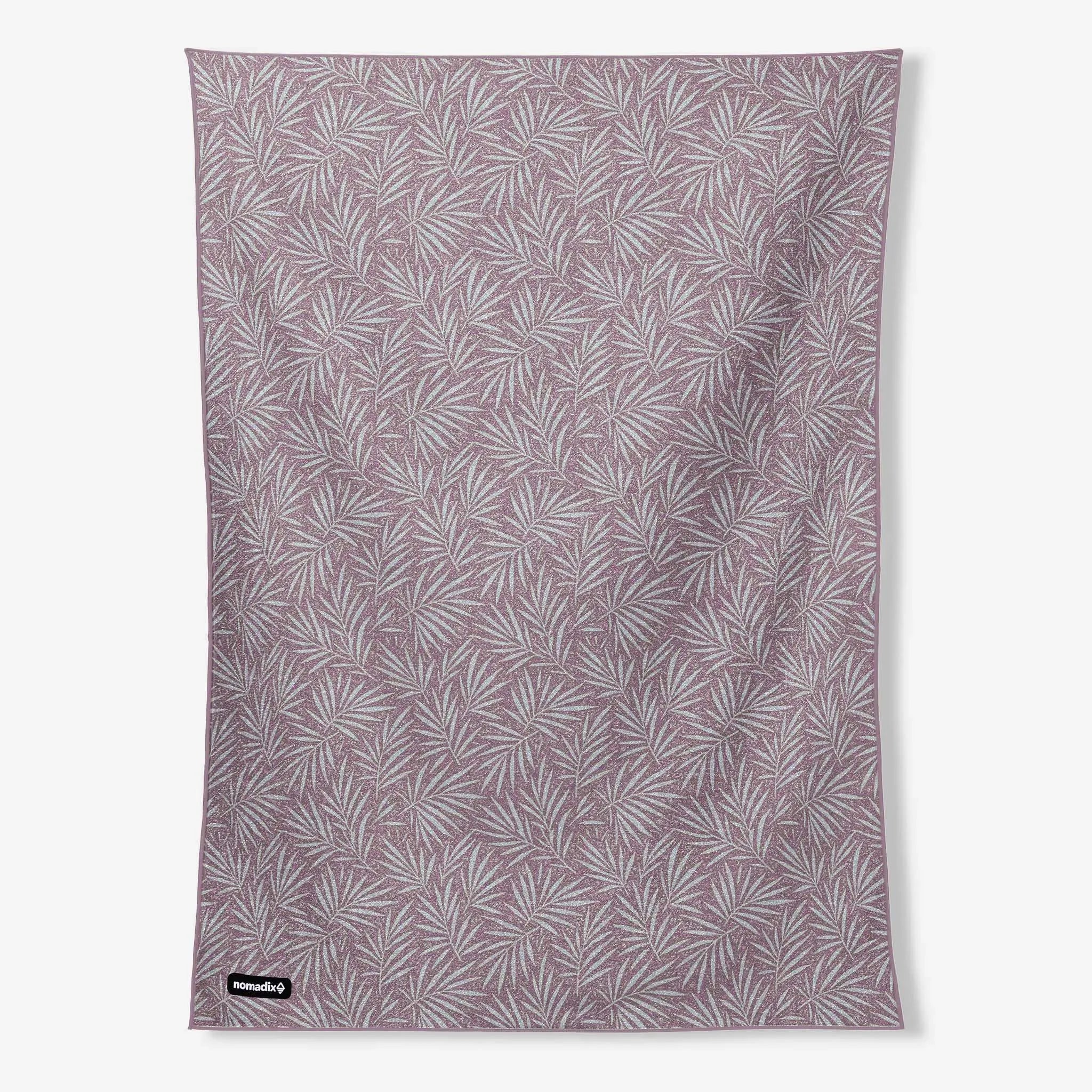 A rectangular fabric towel or blanket with an all-over palm leaf pattern in dusty mauve and white, featuring a small black 'hummus' brand tag in the bottom-left corner, shown against a plain light gray background.