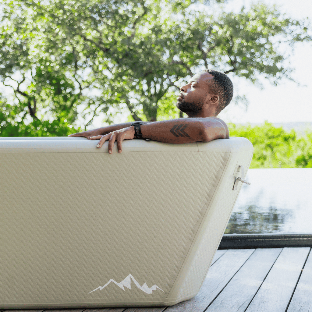 Man relaxing in a portable hot tub outdoors with trees in the background