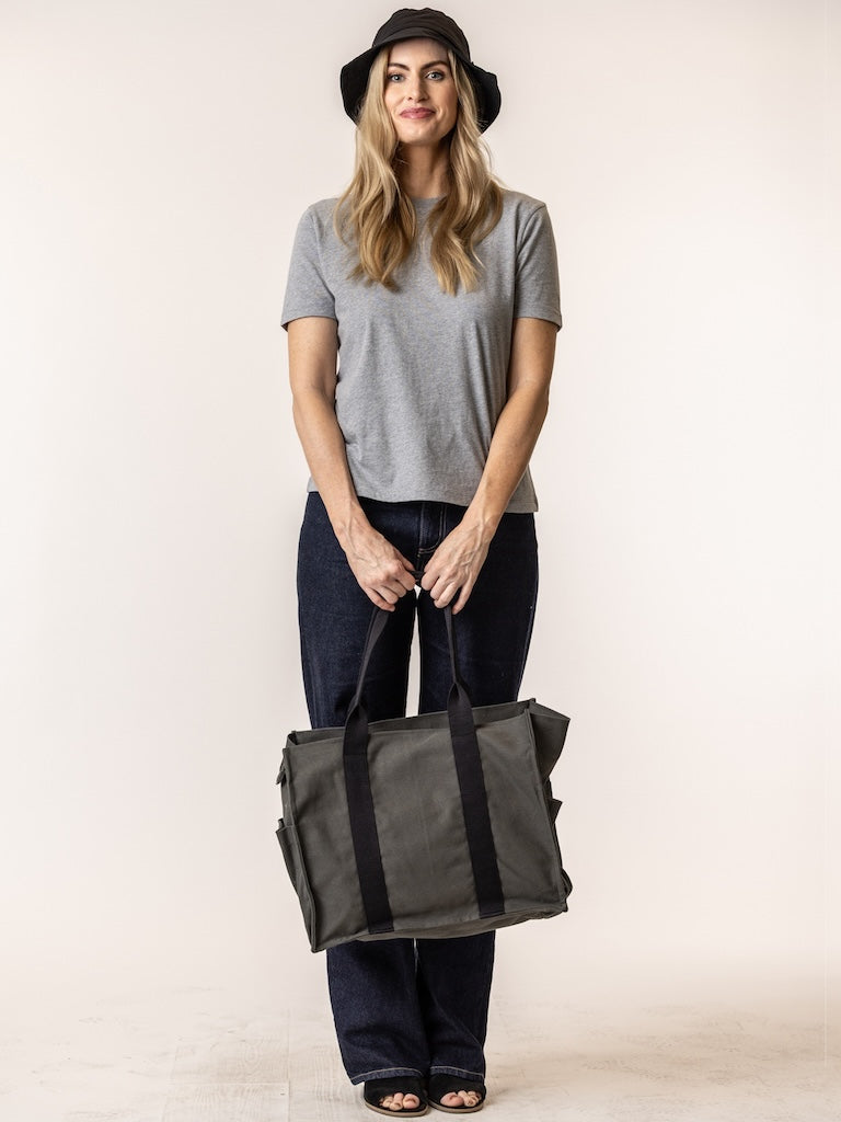 Woman holding a black tote bag against a plain background