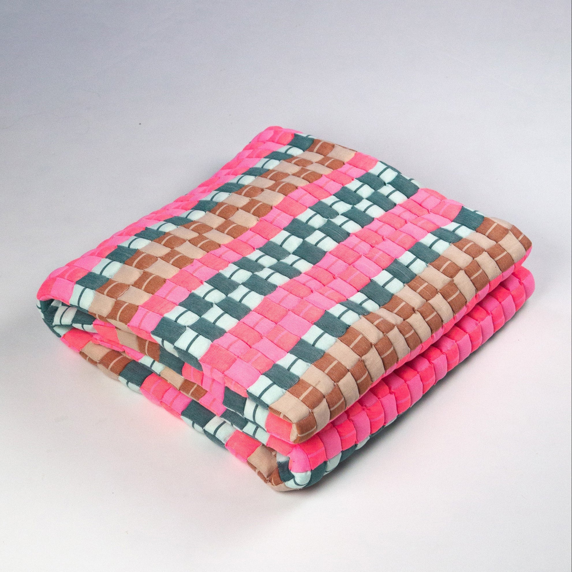 Colorful woven mat with pink, green, and brown pattern on a light gray background
