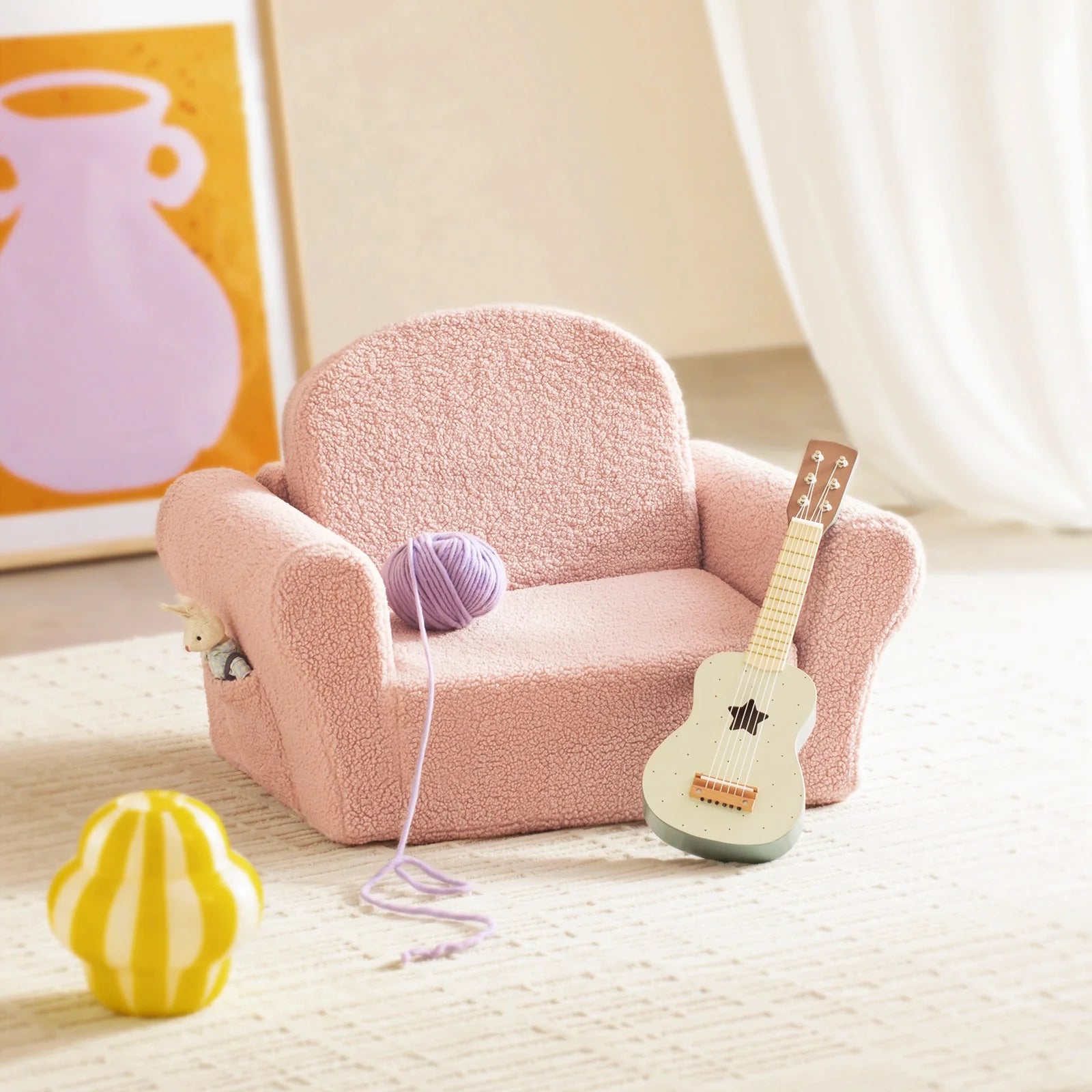 Pink plush chair with a guitar, yarn ball, and lemon toy on a light wooden floor.