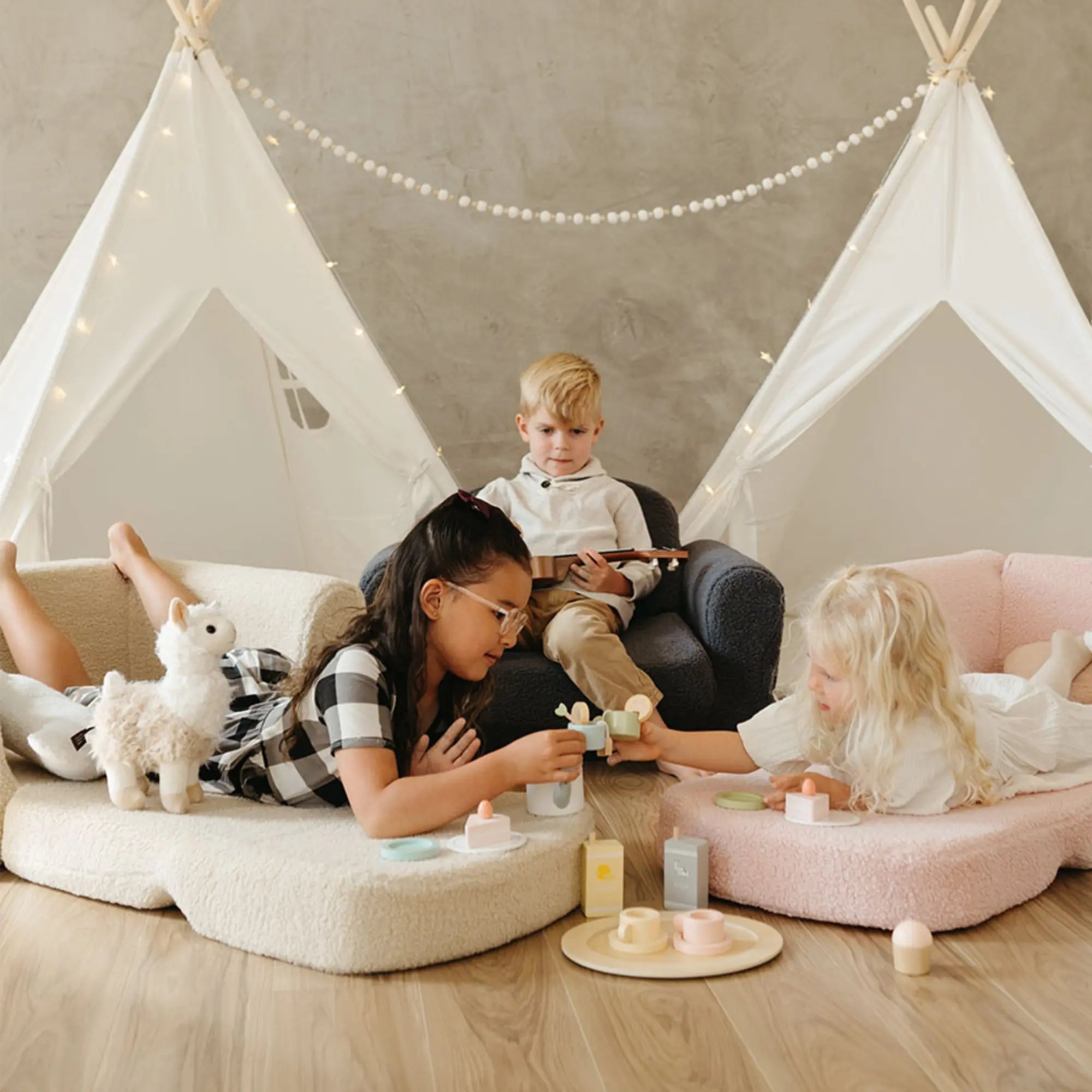 Children playing in a room with teepee structures and toys on the floor.