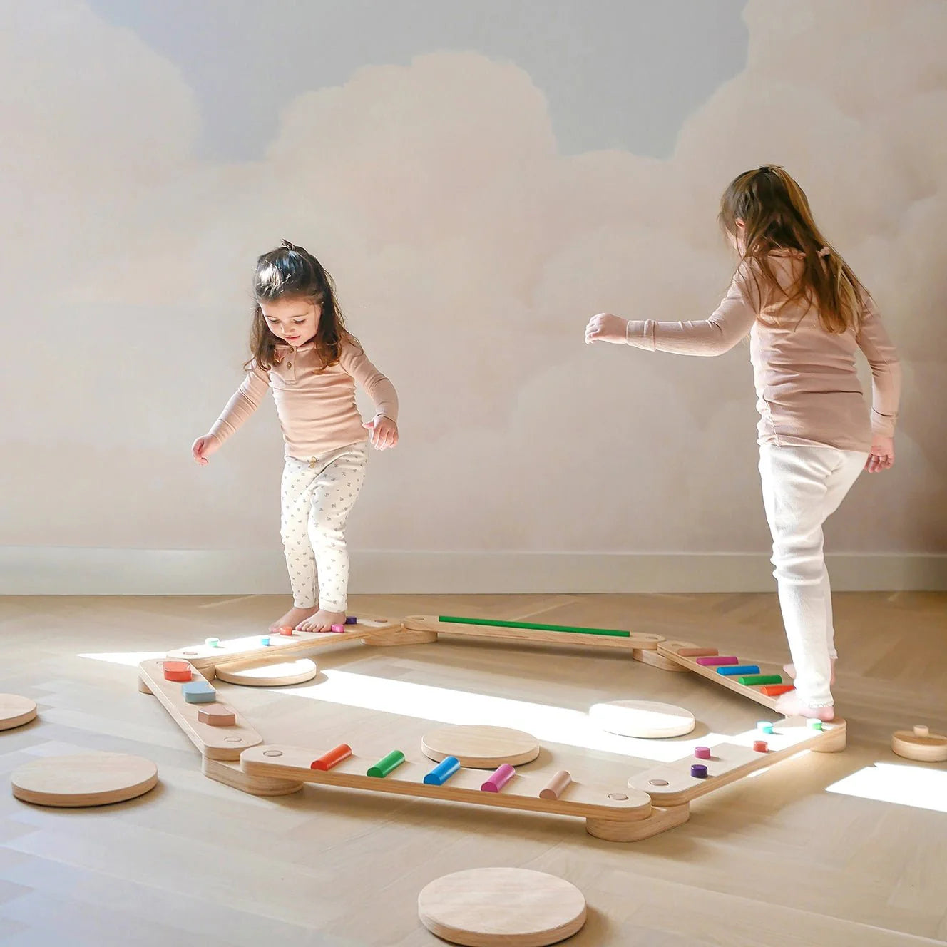 Two children playing with a wooden balance beam toy on a light wood floor.