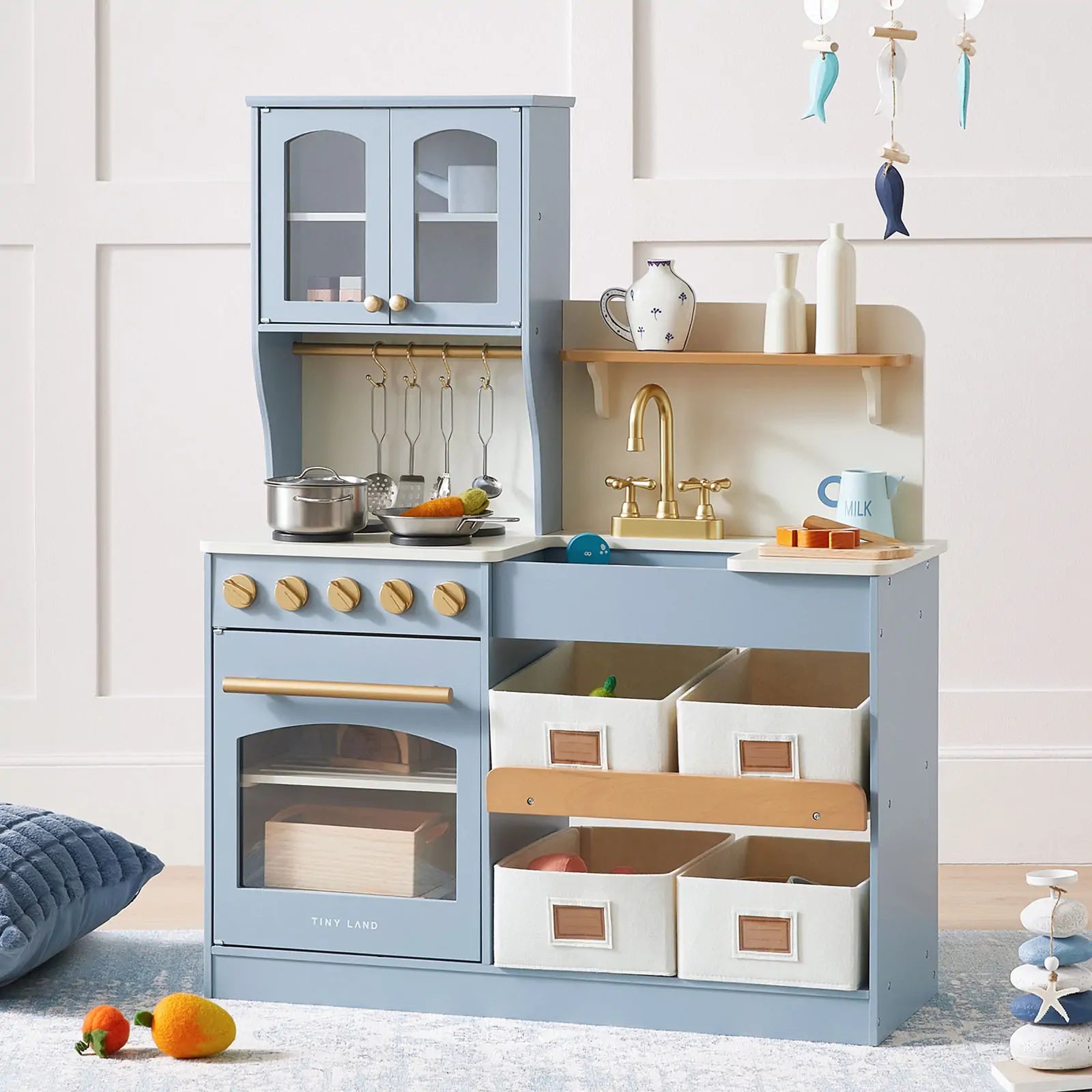Children's play kitchen set with blue cabinets, wooden shelves, and various accessories on a light background.