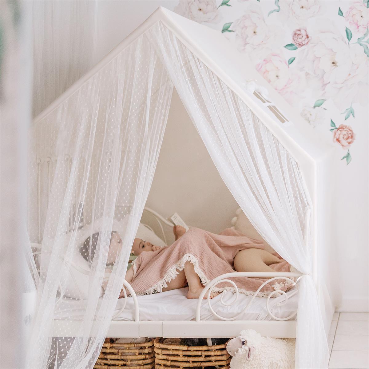 Child lying in a white canopy bed with floral wallpaper in the background