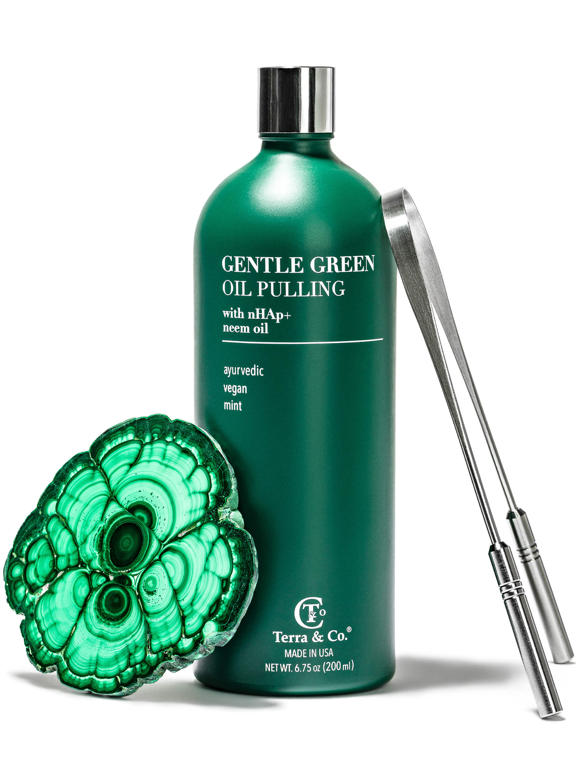 Green bottle of 'Gentle Green Oil Pulling' with a green stone and metal tool on a white background