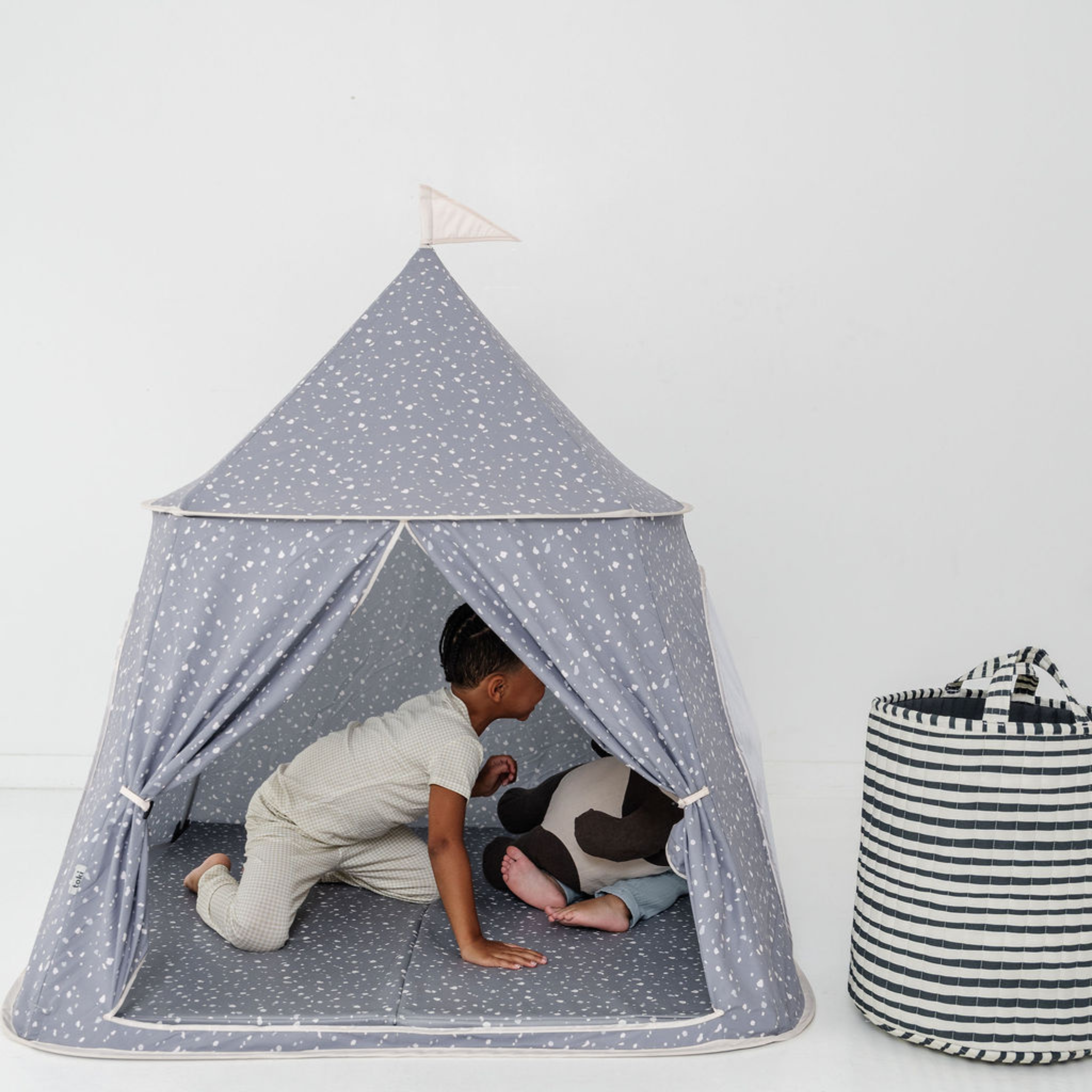 Children playing inside a gray tent with white polka dots on a white background
