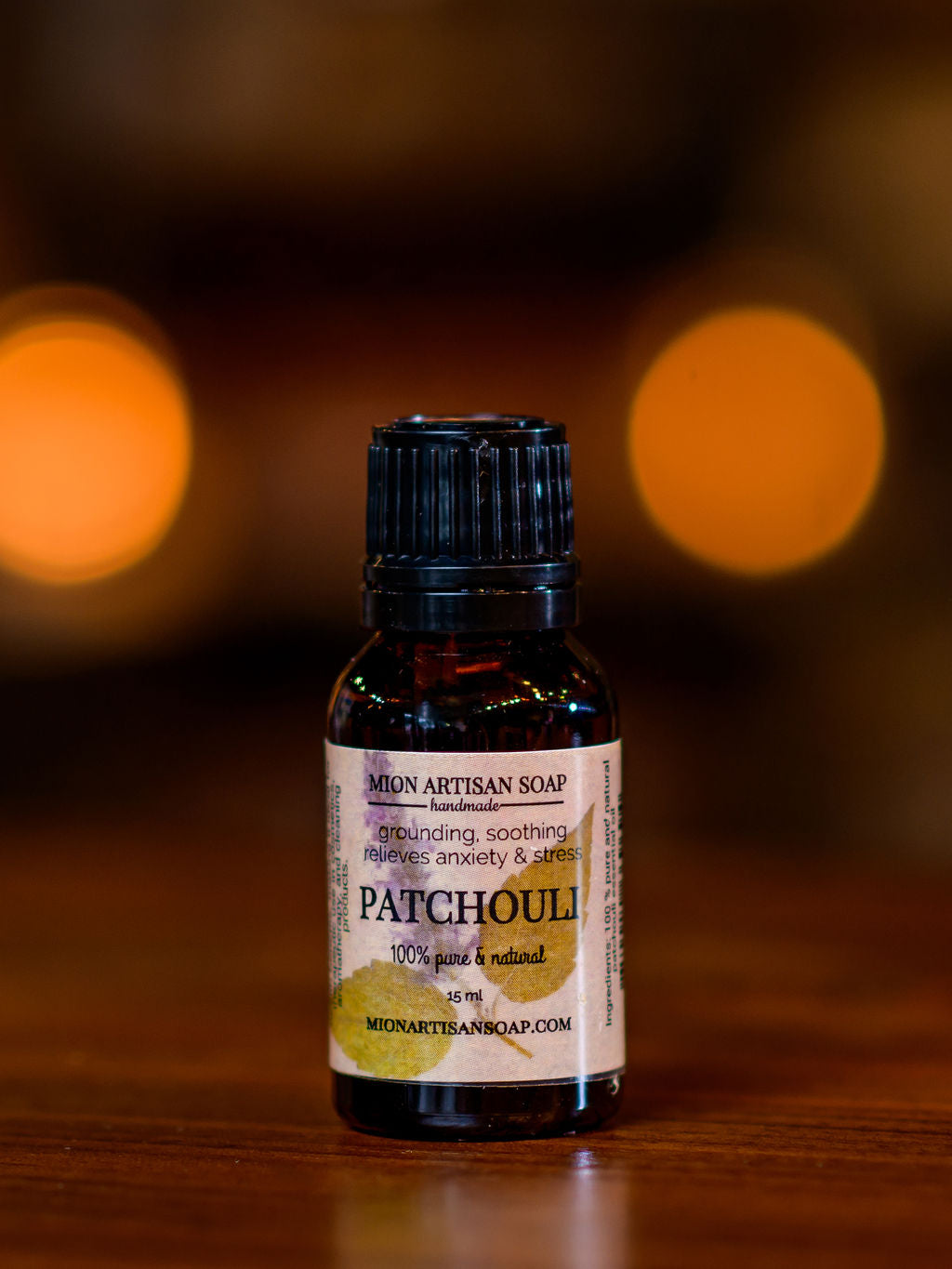 Patchouli essential oil bottle on a wooden surface with blurred lights in the background