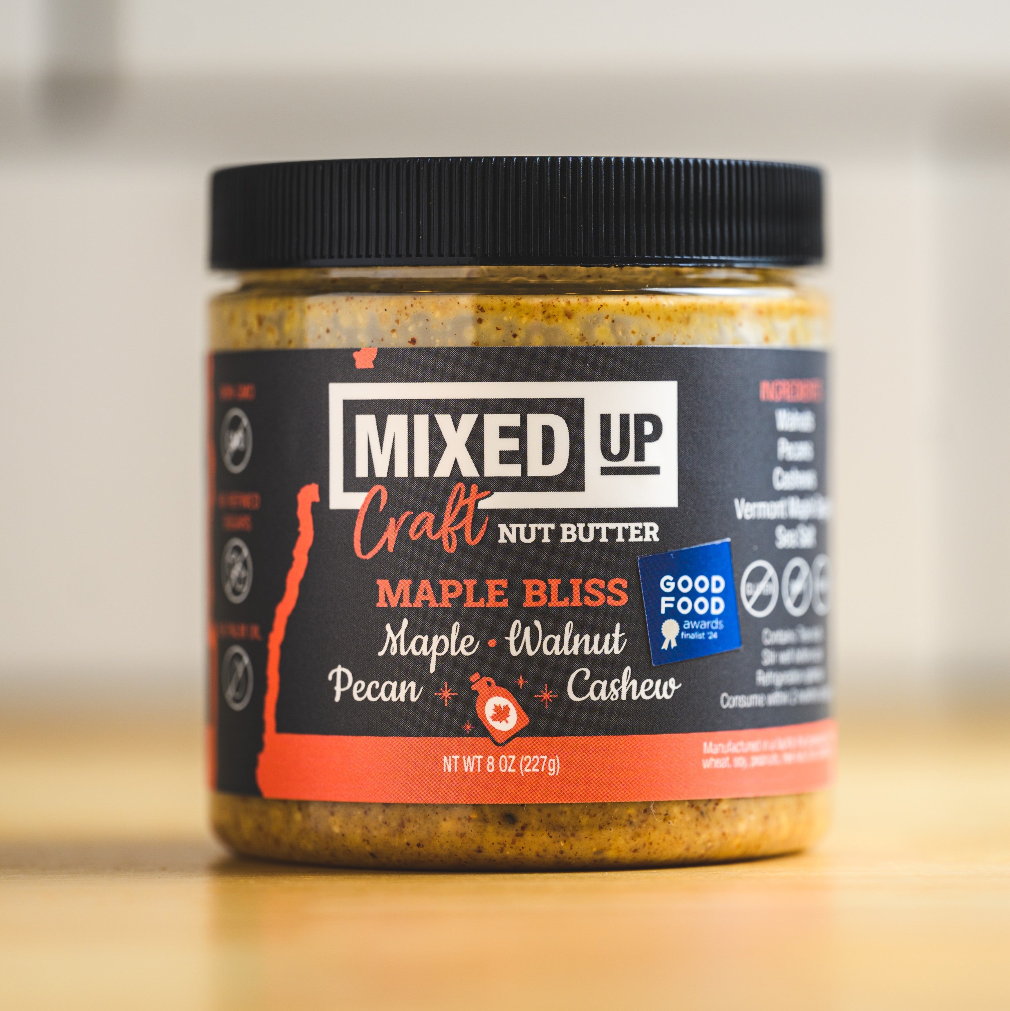 Jar of Mixed Up Craft Nut Butter with a black lid on a wooden surface