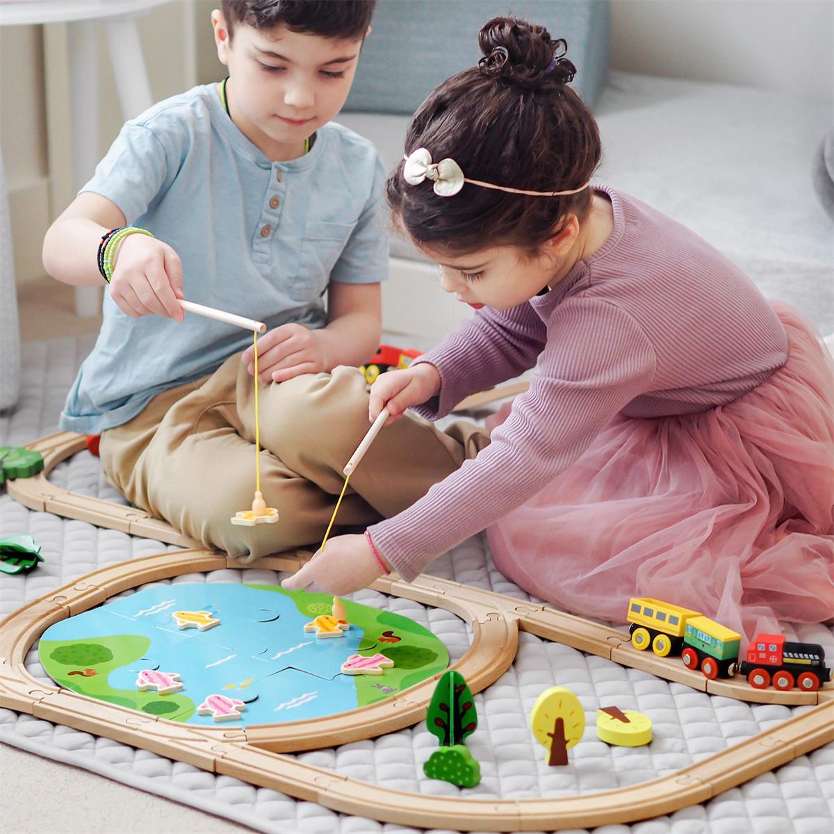 Two children playing with a wooden train set on a mat.