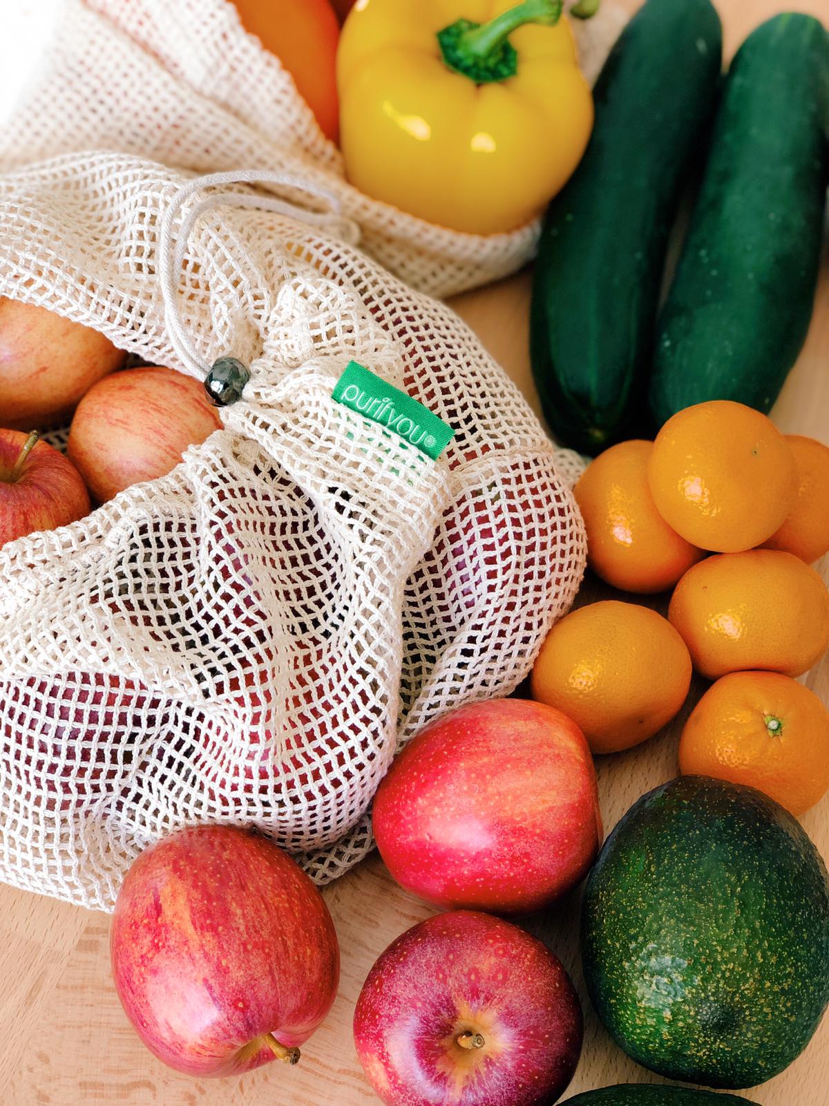 Fruits and vegetables including apples, oranges, and cucumbers on a wooden surface with a reusable mesh bag.