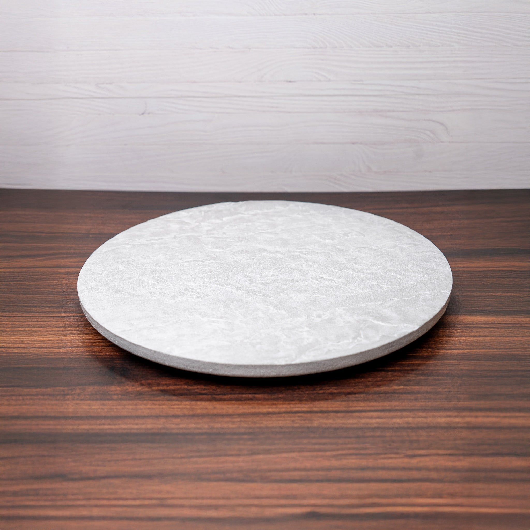 Round white stone slab on a wooden surface with a white brick wall background