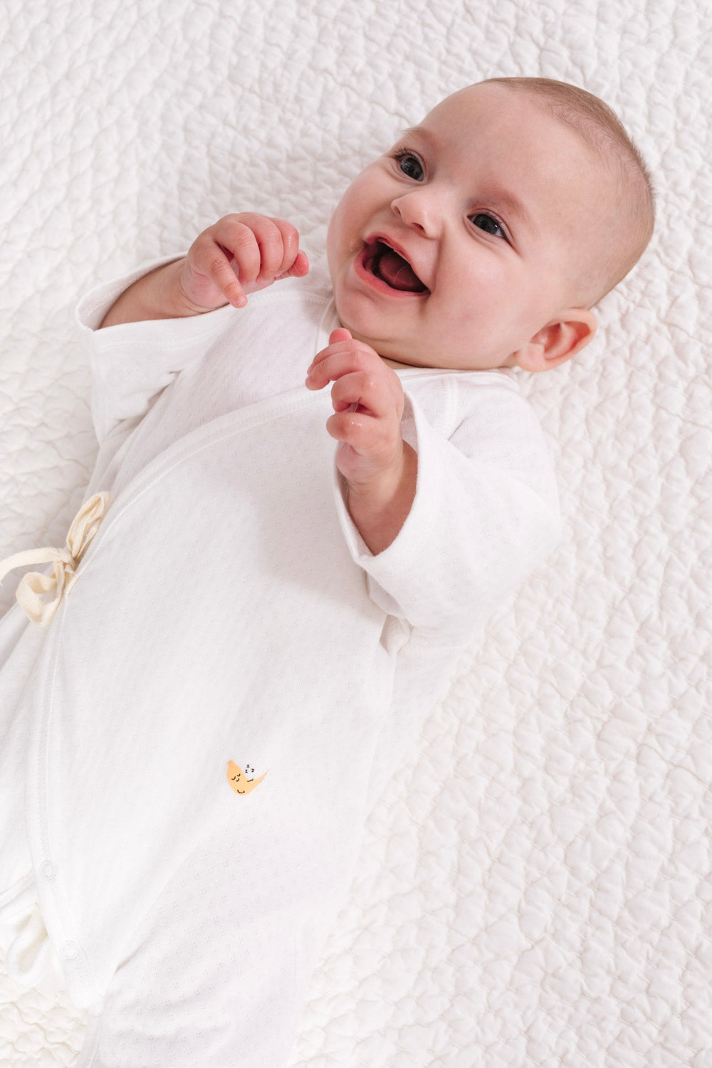 Baby wrapped in a white blanket on a textured white surface