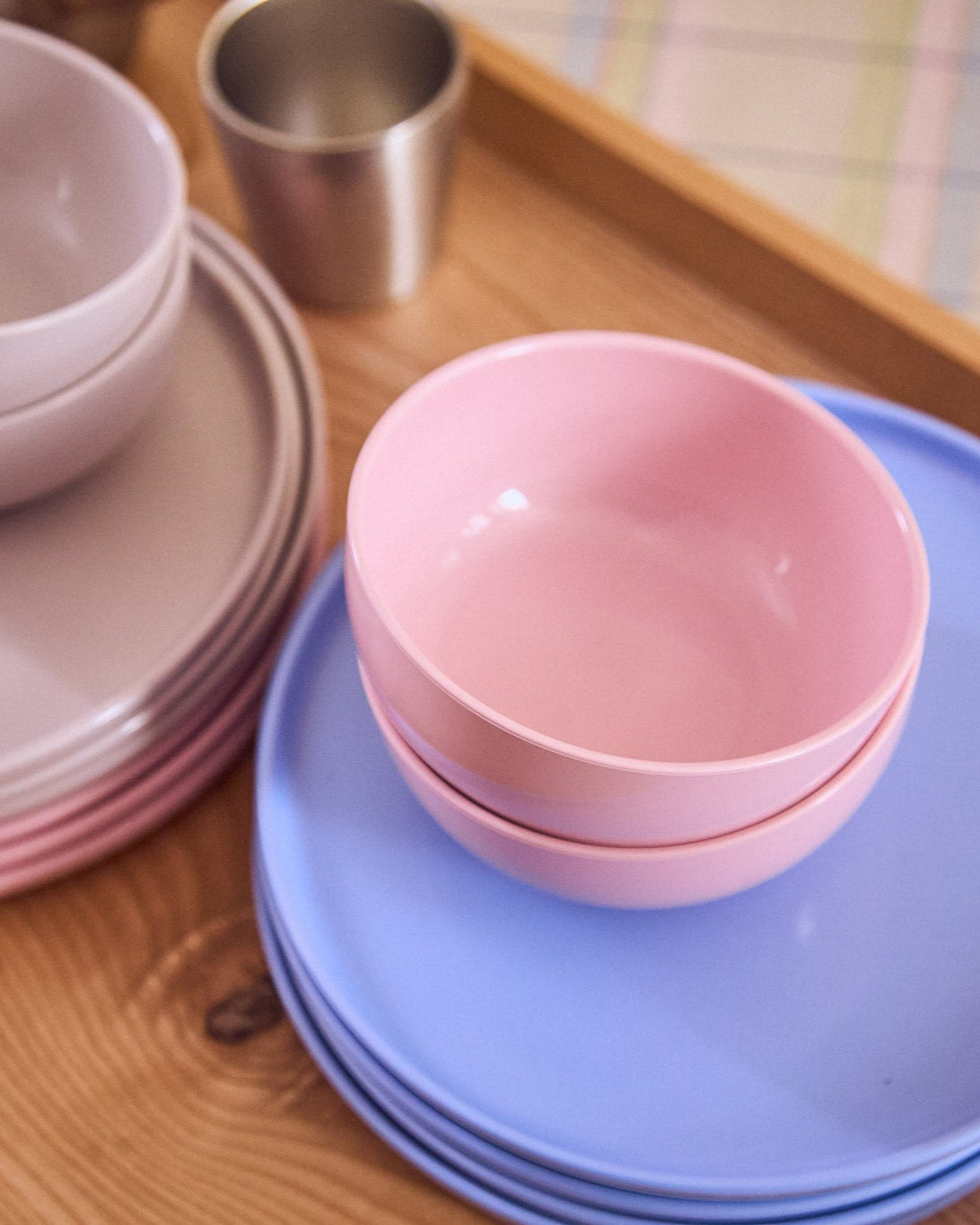 Stacked pink bowls on a blue plate with a wooden surface and metal cup in the background.