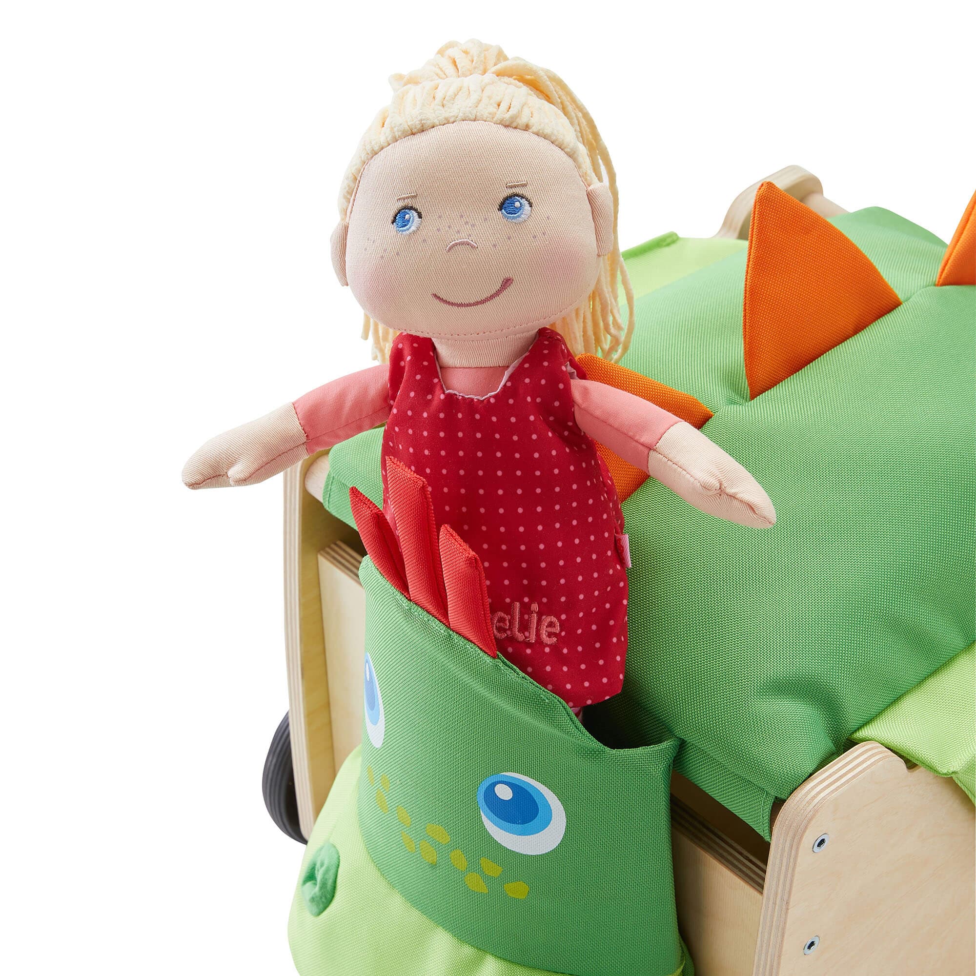 Toy doll with blonde hair and blue eyes sitting on a green dinosaur-shaped toy.