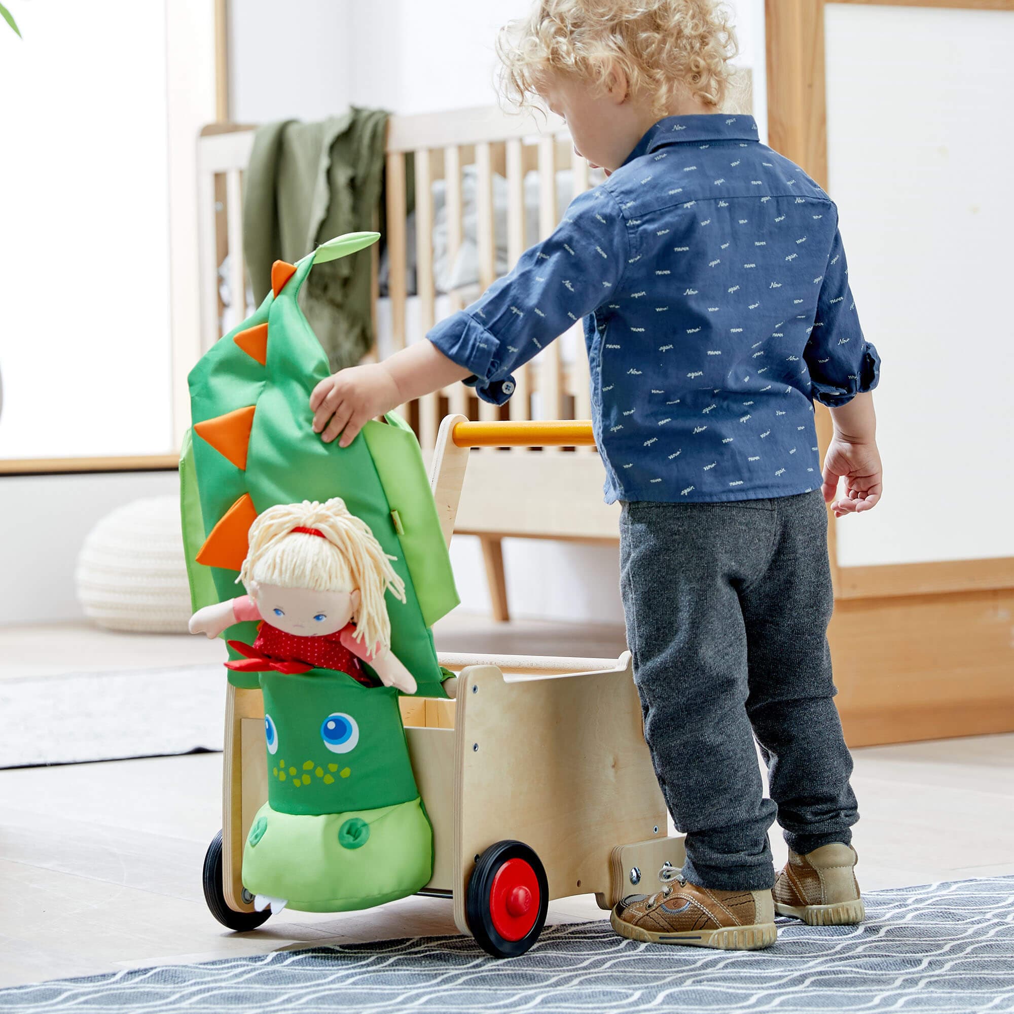 Child playing with a green toy dinosaur in a room with a crib and wooden floor.