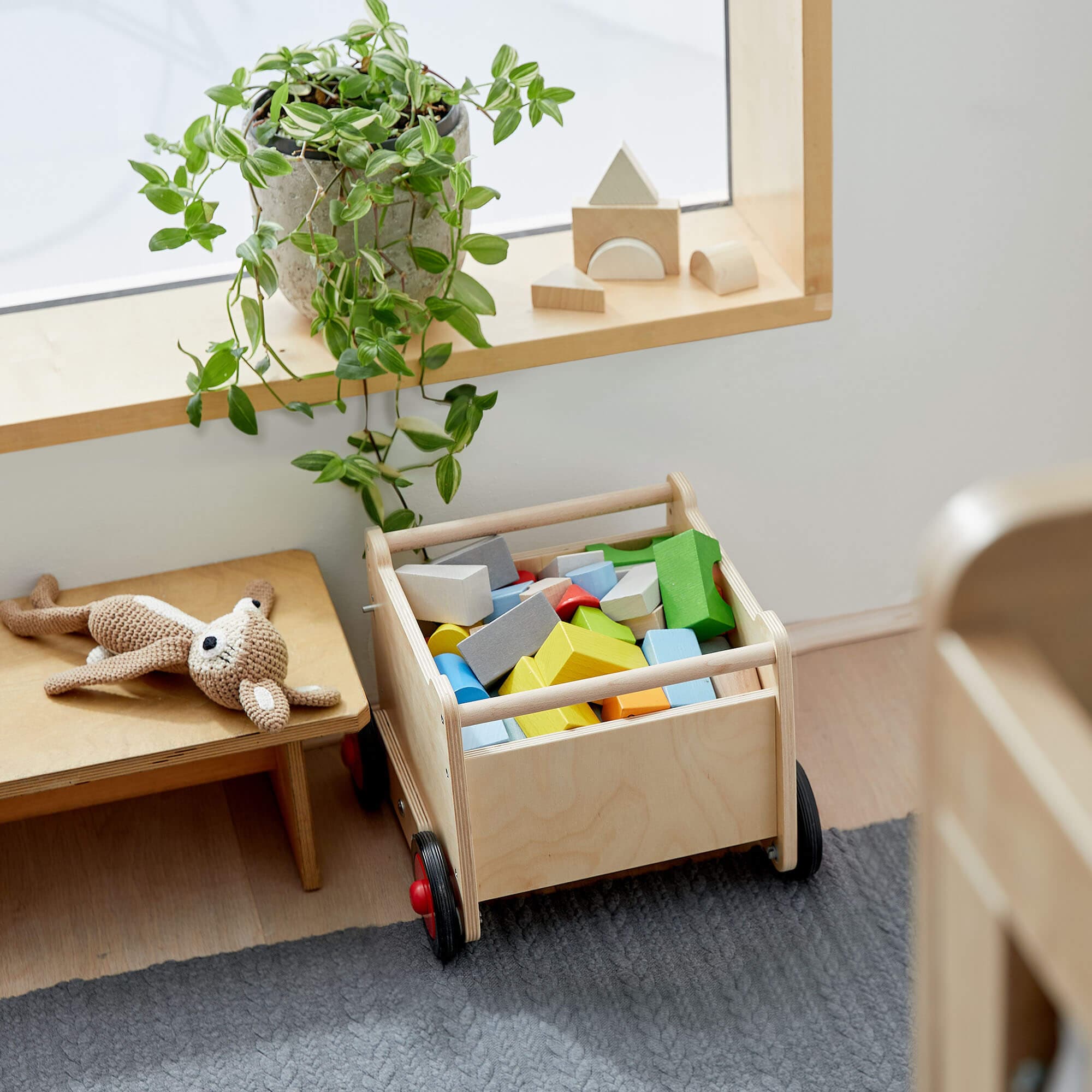 Wooden cart with colorful blocks in a room with a shelf and plant