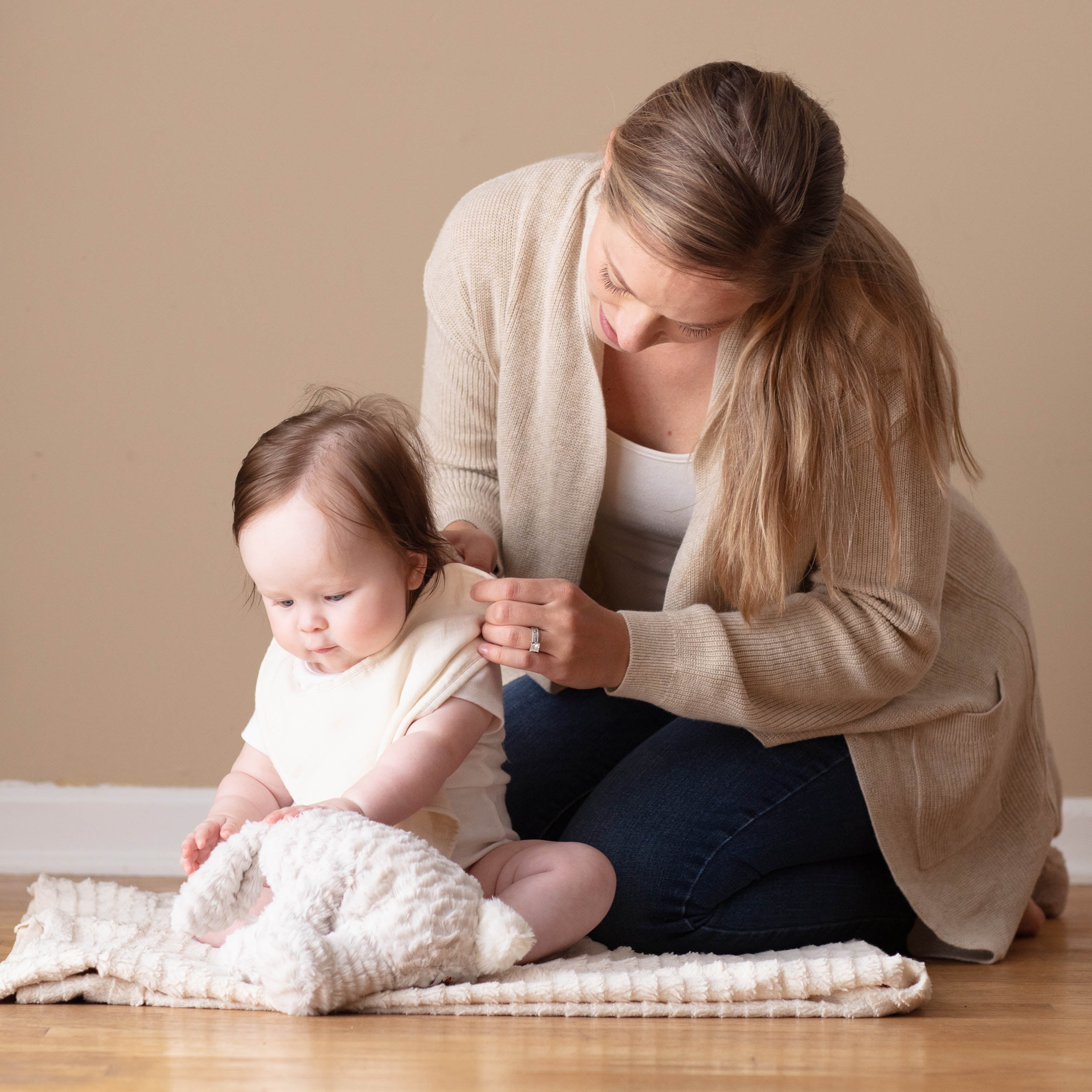 Woman and child sitting on a wooden floor with a beige wall background