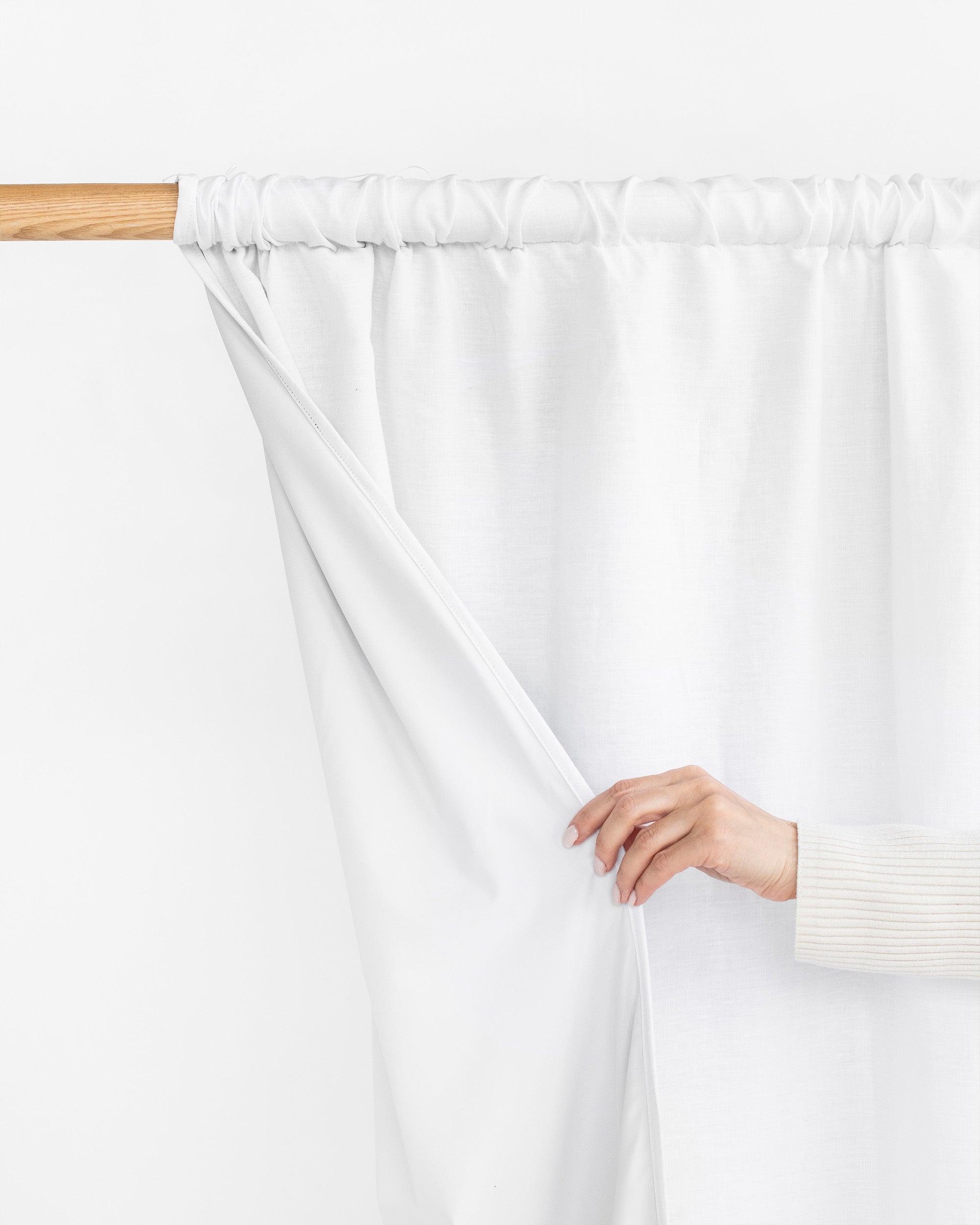 White curtain being held by a hand against a white background