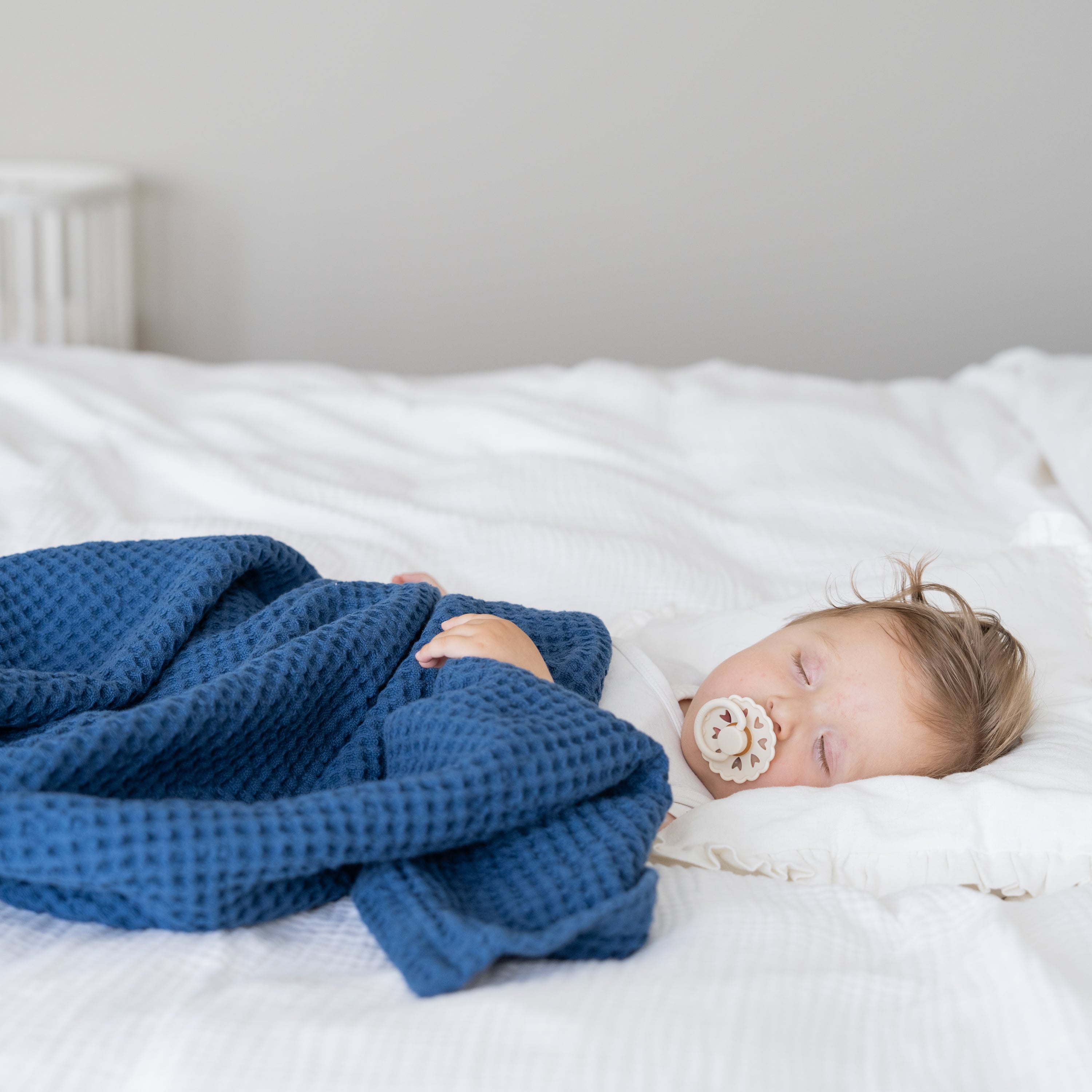 Baby sleeping on a bed with a blue blanket and white pacifier