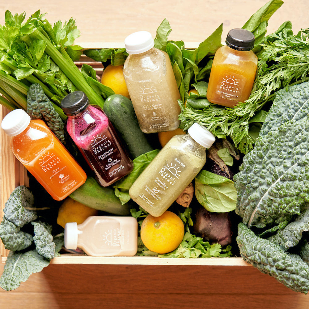 Assorted bottles of organic juice surrounded by fresh vegetables and fruits on a wooden surface.